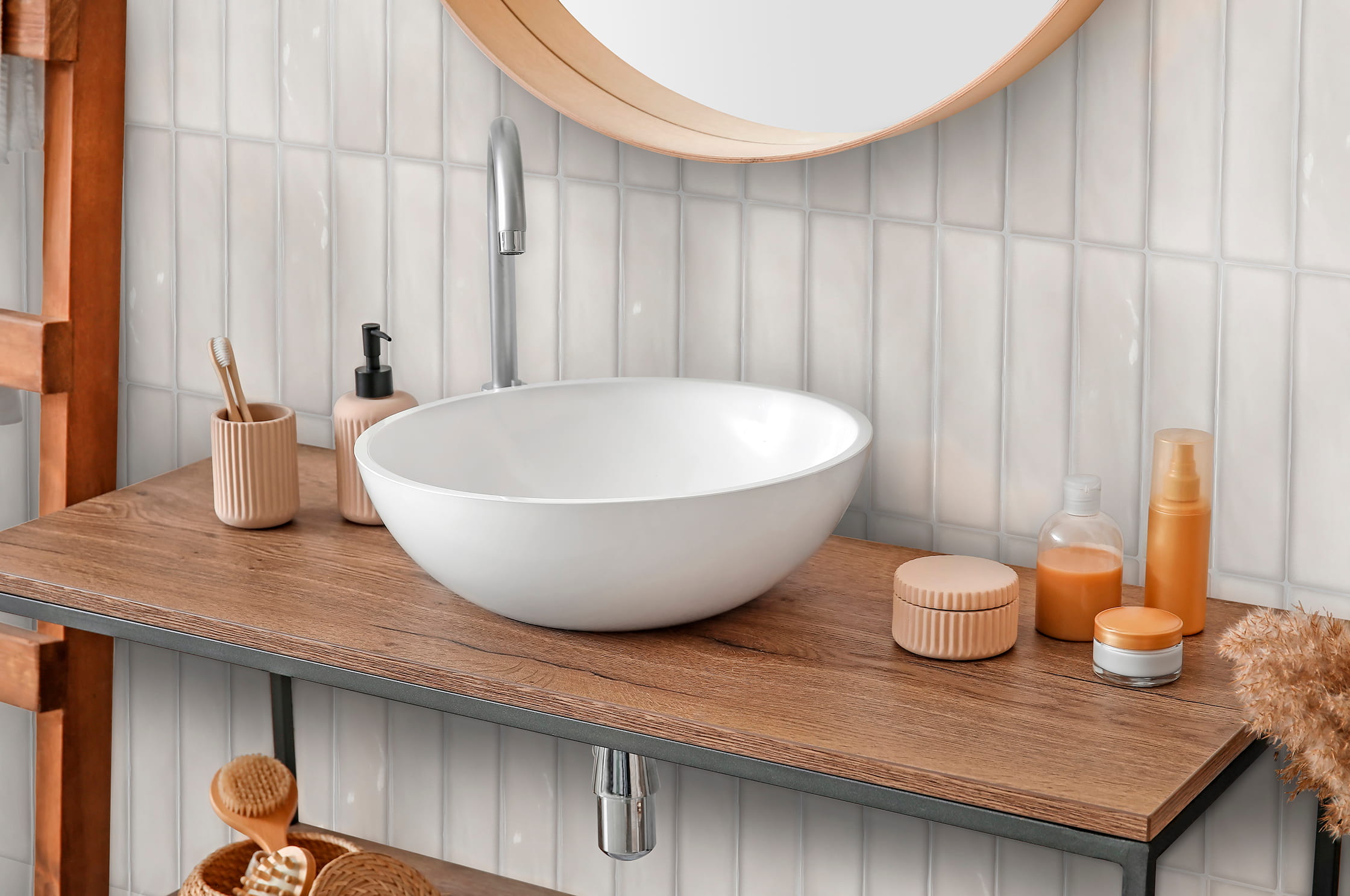 Modern white vessel sink with wood countertop, beige bathroom accessories, and round wooden-framed mirror.