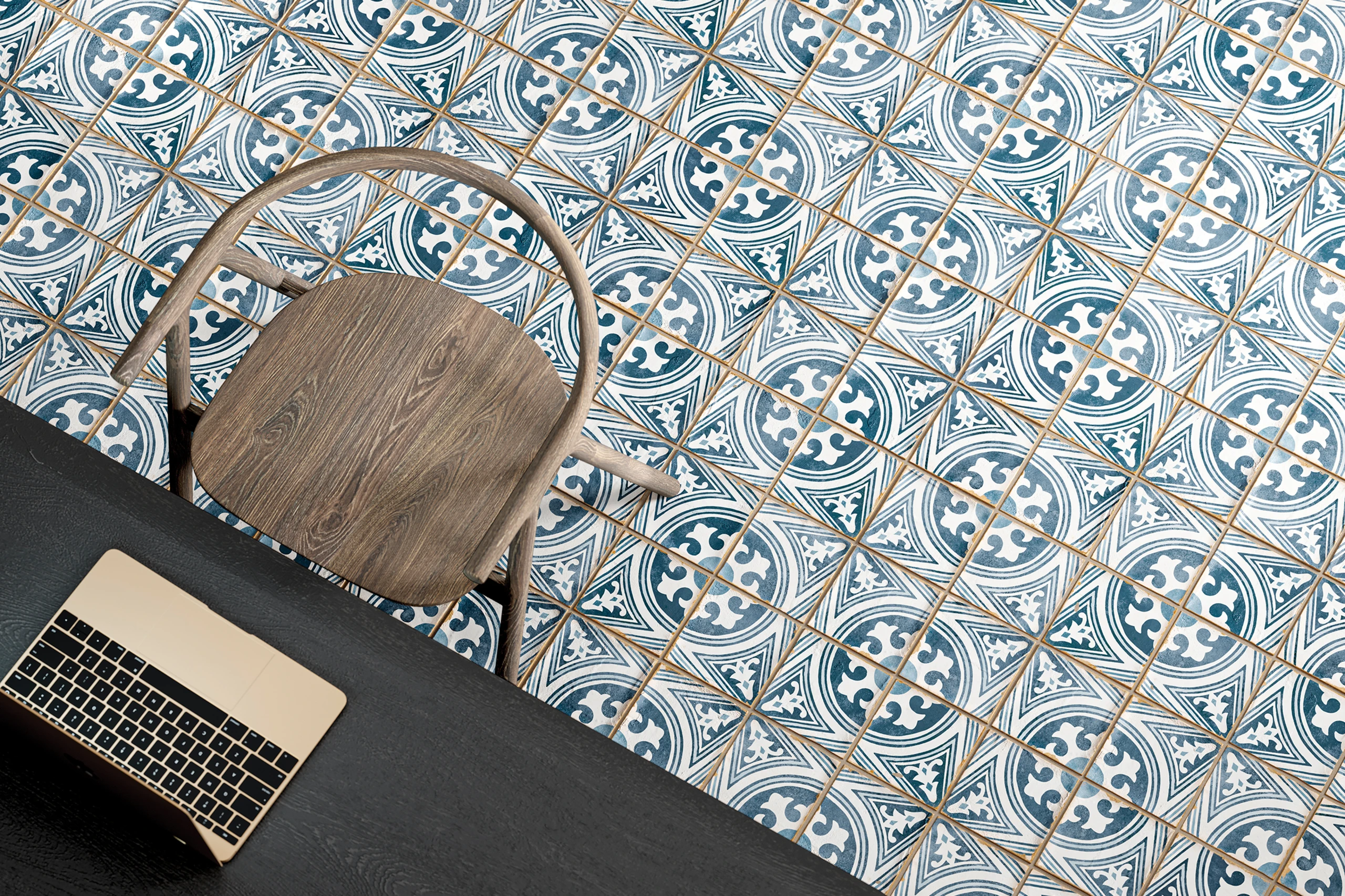 Overhead view of wooden chair, dark table, and blue-white patterned tiled floor with laptop on table.