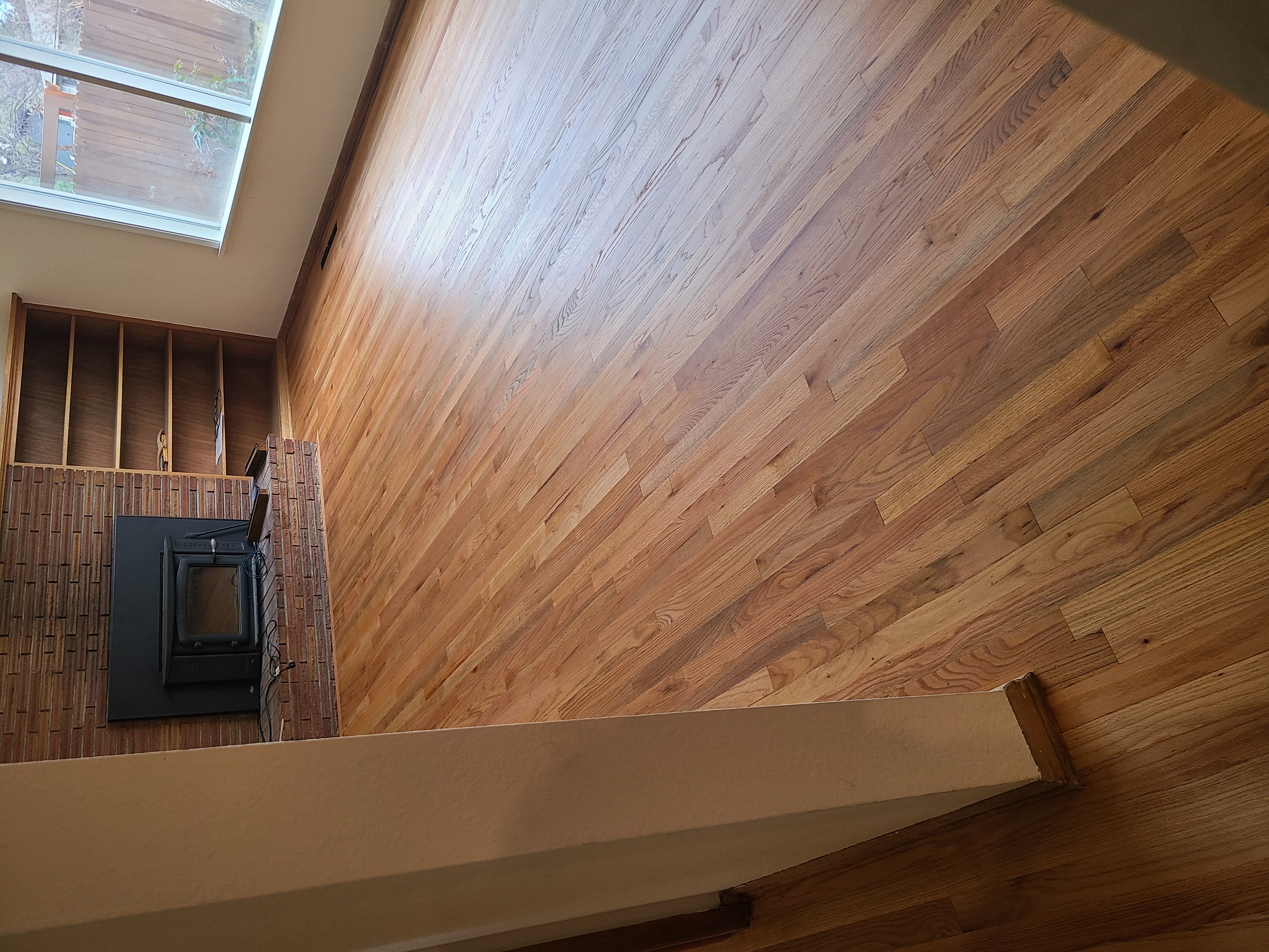 Empty room with polished hardwood floor, brick fireplace, built-in wooden shelves, and large window.