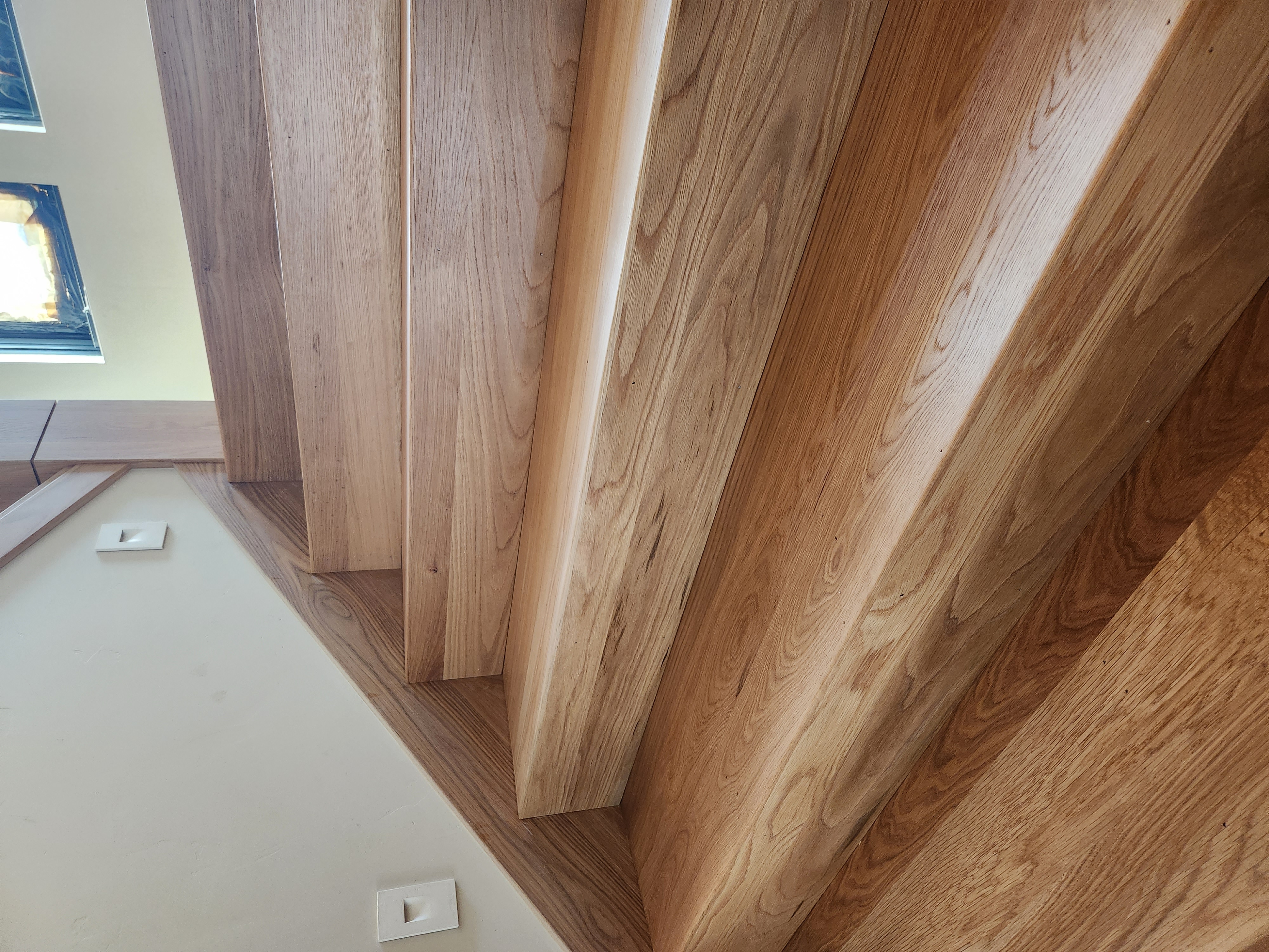 Close-up of polished wooden stairs with natural grain and trim against a beige wall.