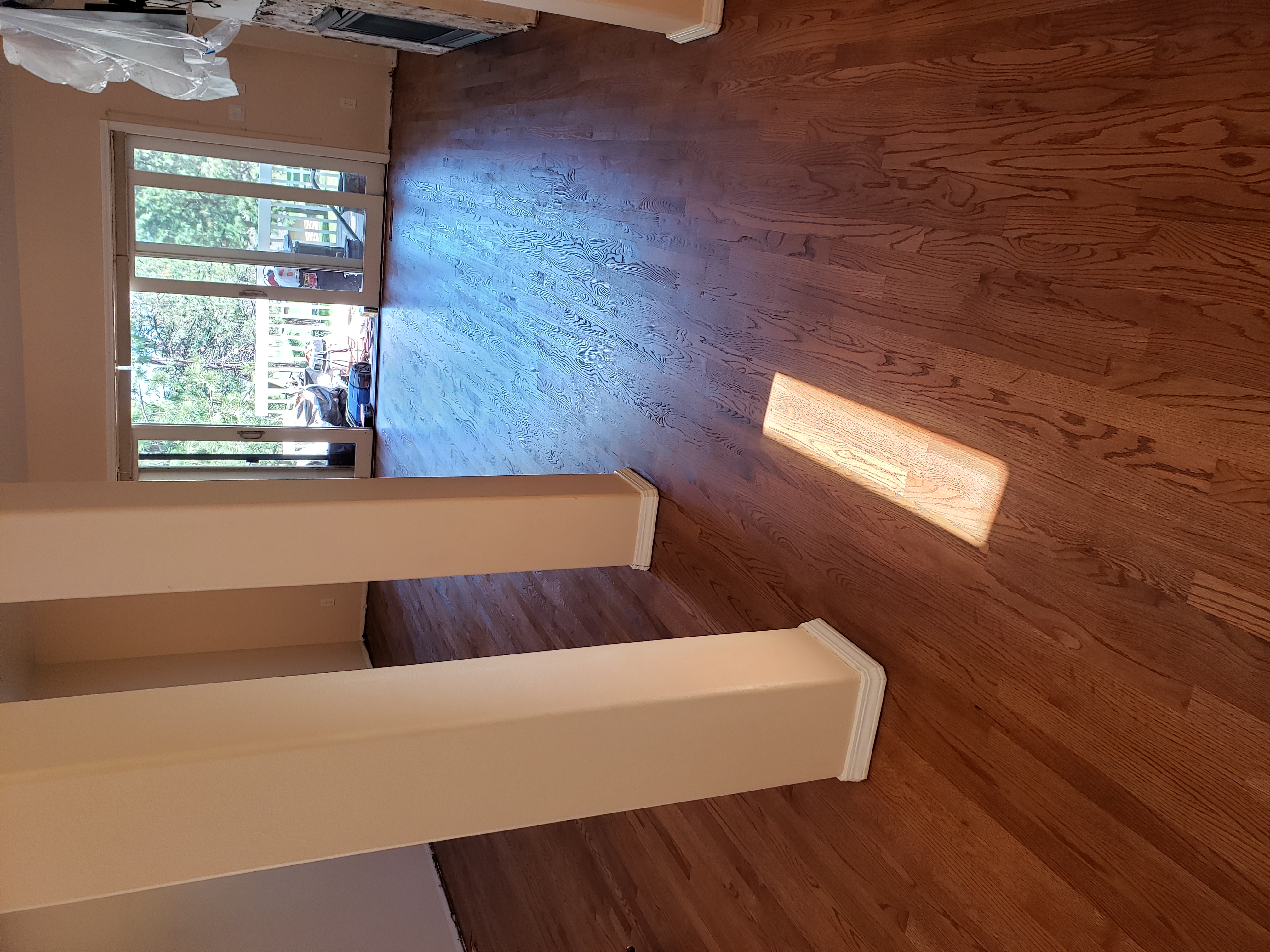 Empty room with brown hardwood floors, beige walls, two pillars, and glass sliding doors to a balcony.