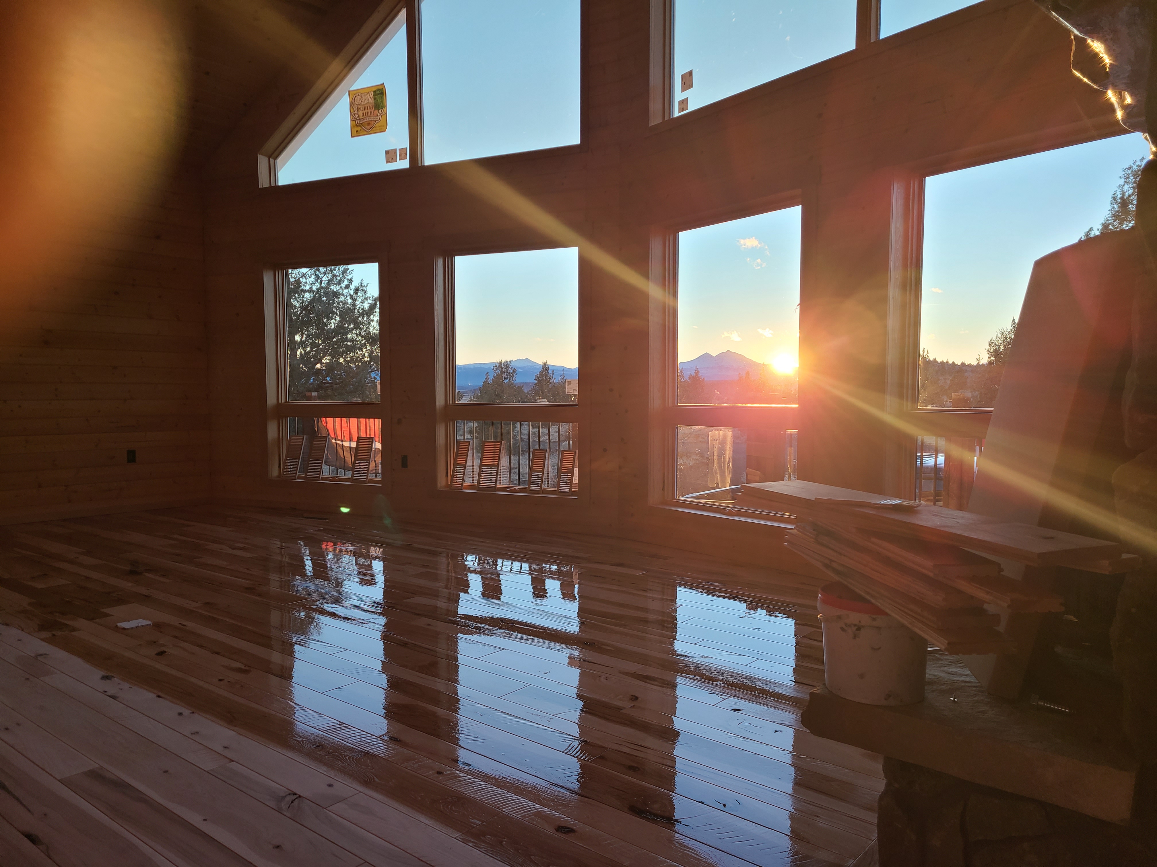 Sunset seen through large windows of a wooden cabin with a shiny hardwood floor reflecting the light.