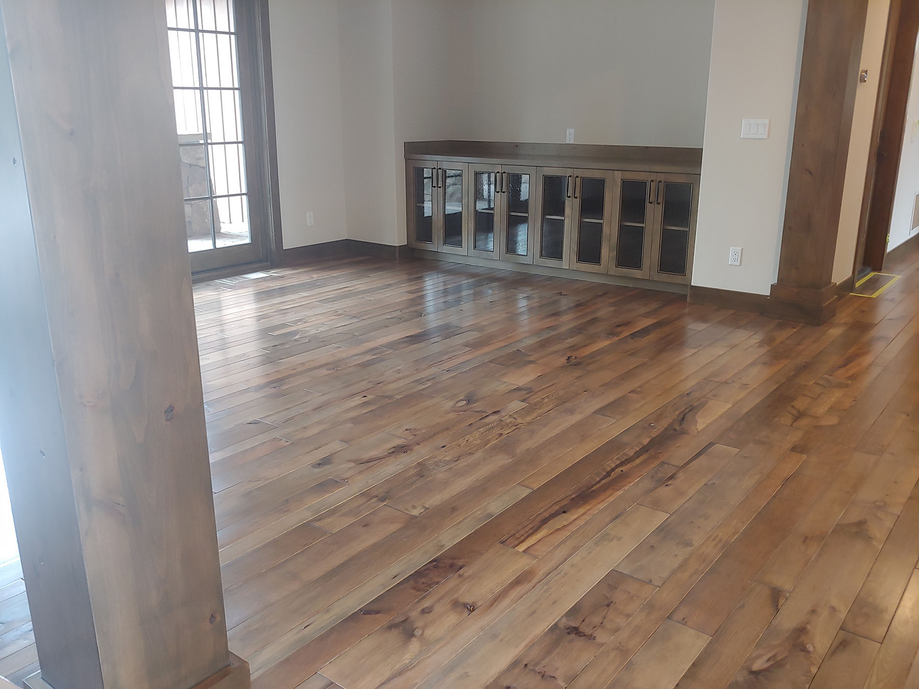 Empty room with polished wooden floor, glass door, and built-in cabinet with glass doors.