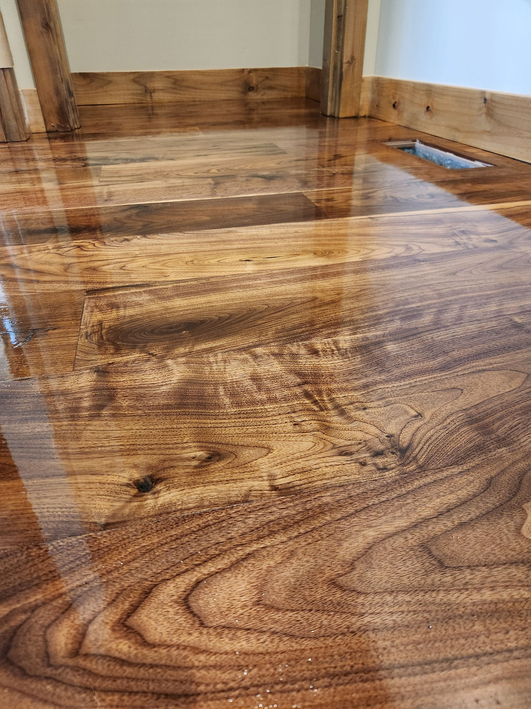 Glossy polished hardwood floor with visible wood grain and baseboard trim in a room corner.