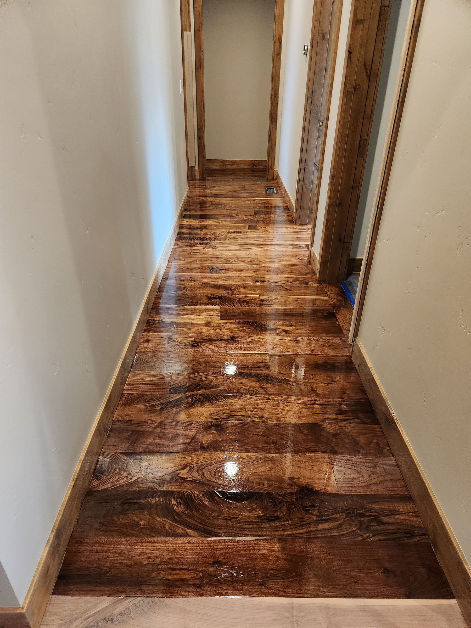 Shiny polished wooden floor in a narrow hallway with open doorways on the right side.