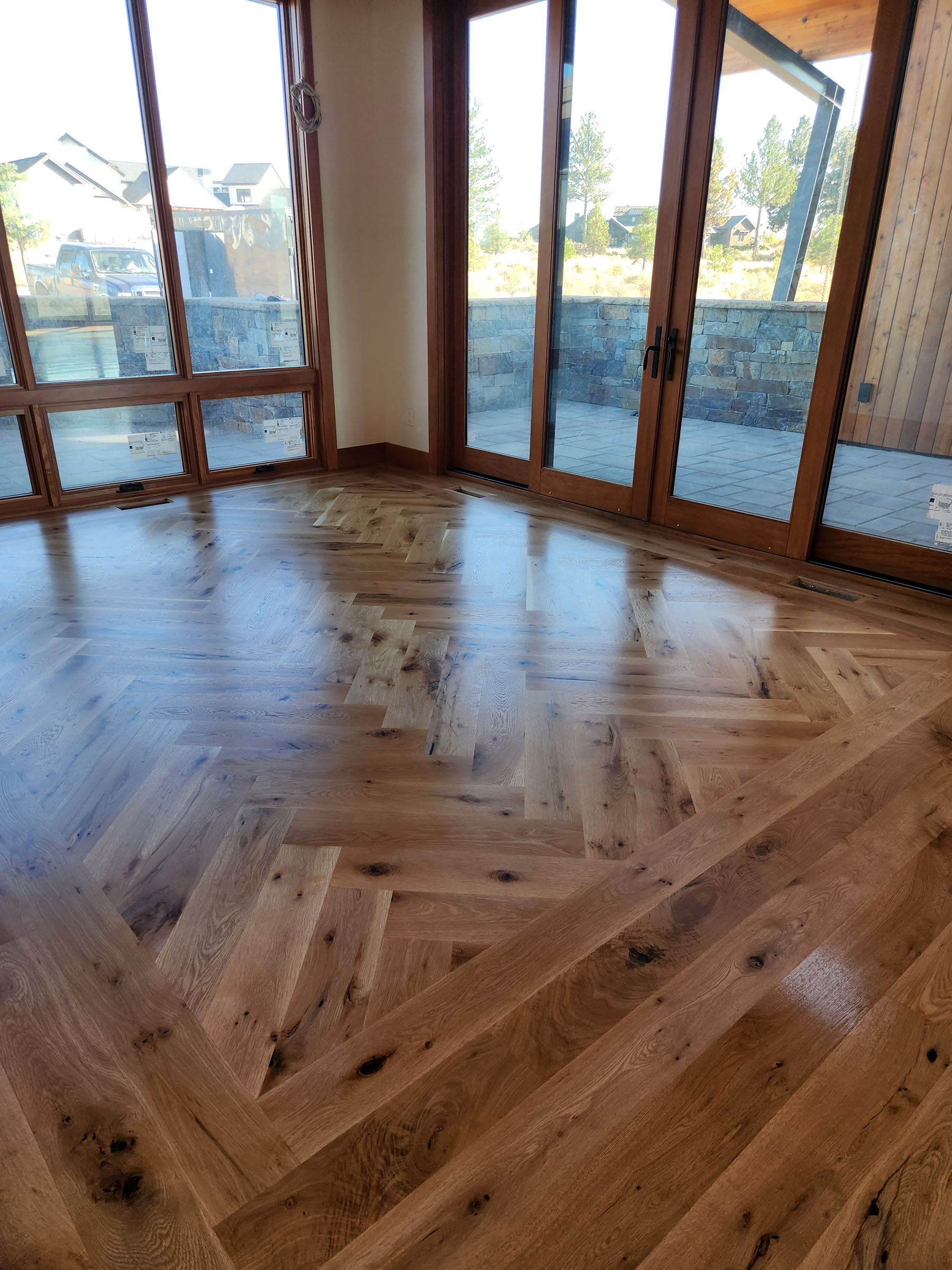 Room with large wooden framed windows and herringbone-patterned wooden floor.