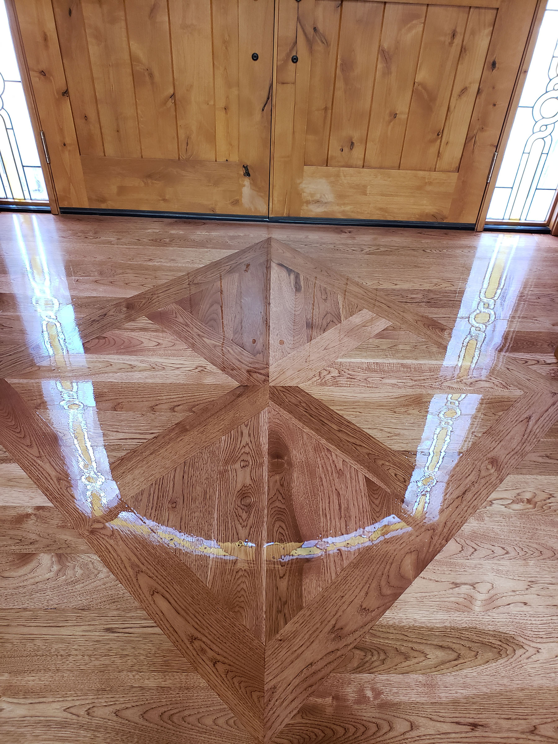 Glossy hardwood floor with an inlaid geometric diamond pattern reflecting stained glass windows