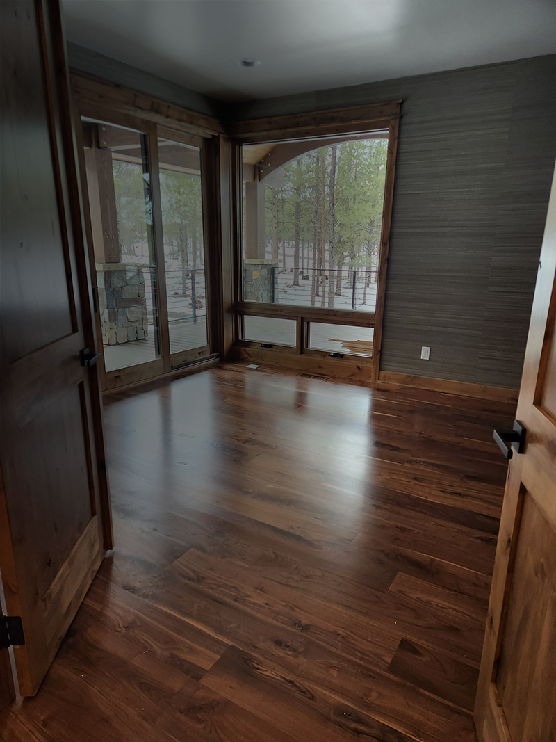 Empty room with wooden floors, large windows, and a view of trees outside.