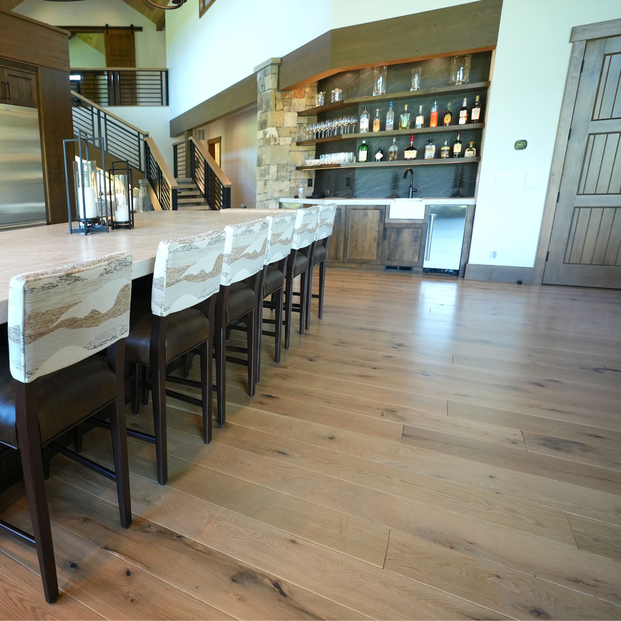 Modern kitchen island with six patterned bar stools and a stocked home bar in the background.