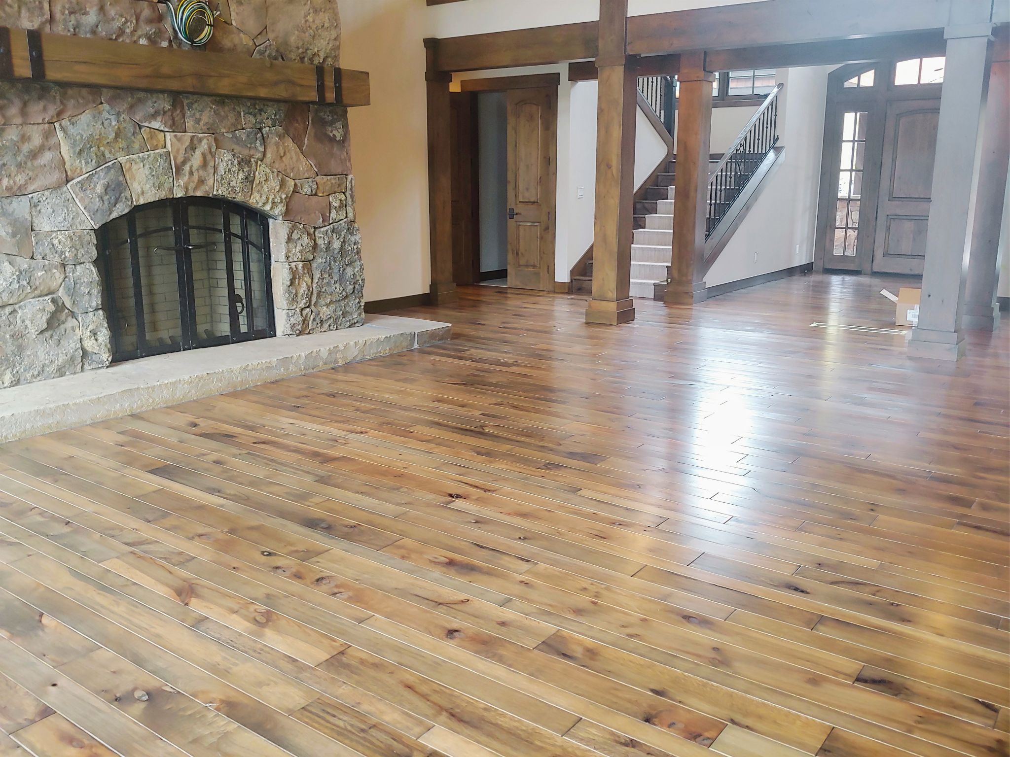 Empty living room with wooden floor, stone fireplace, wooden pillars, stairs, and front door.