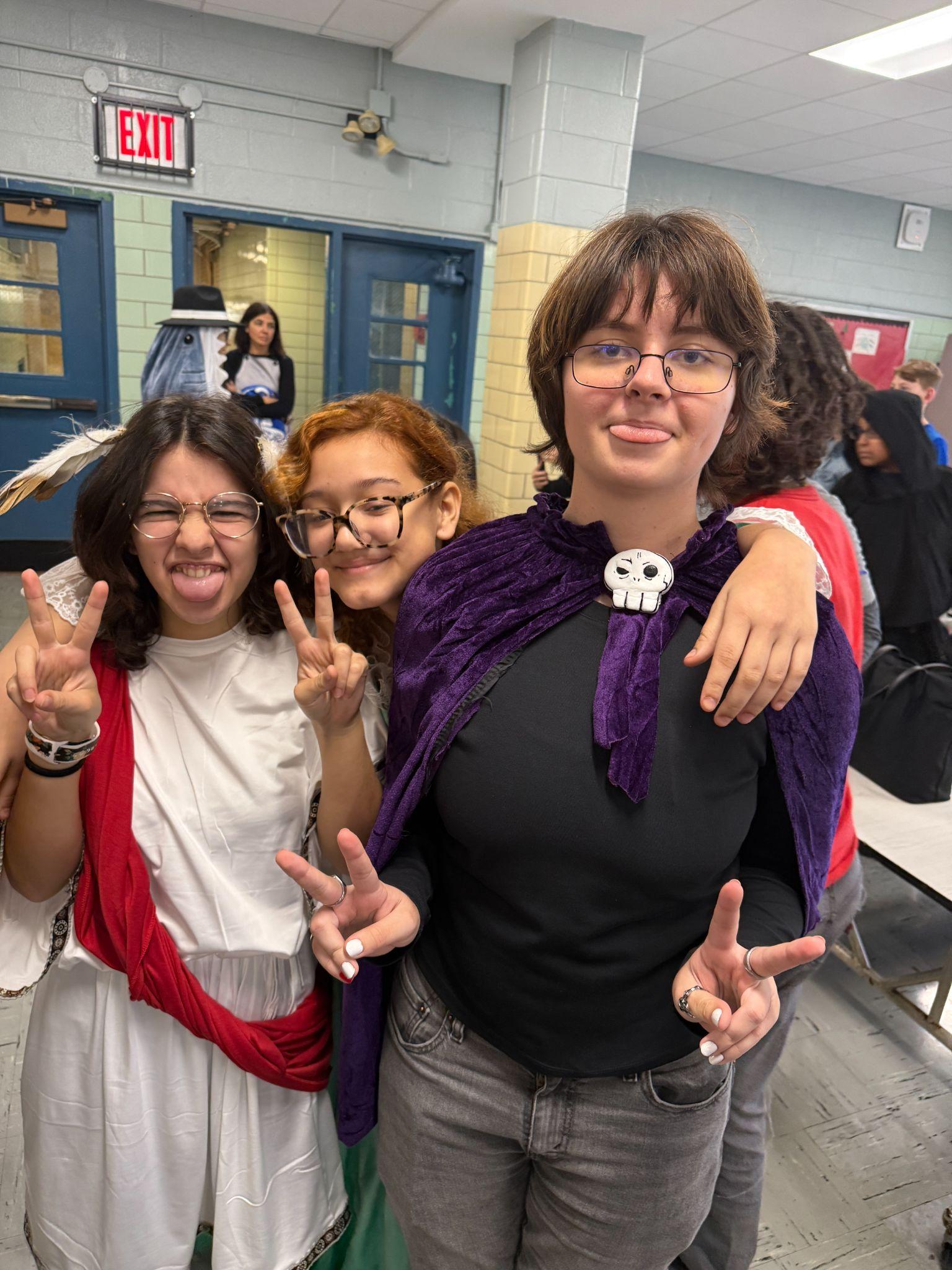 Three students in Halloween costumes posing together in school cafeteria
