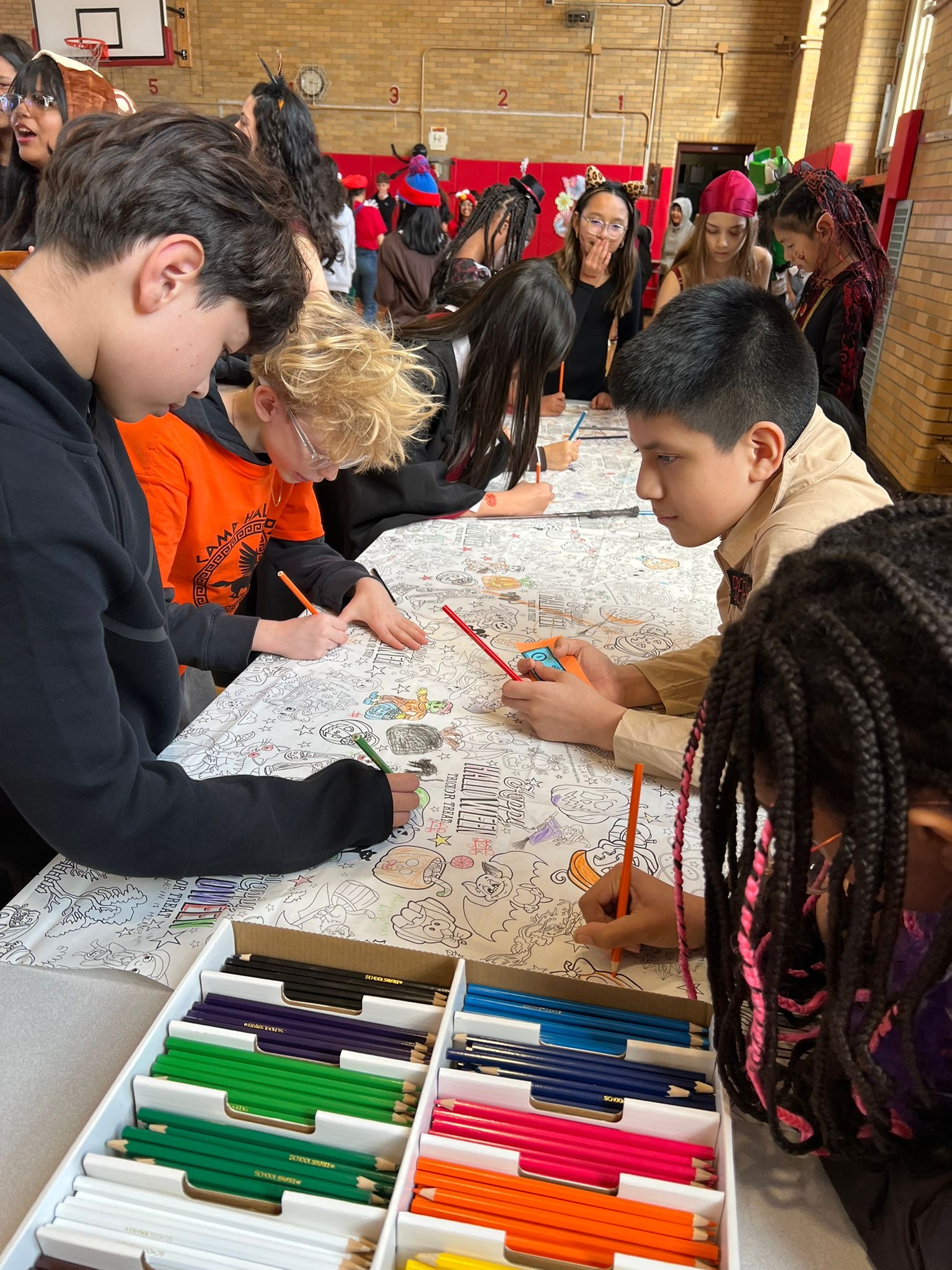 Students coloring a large shared Halloween mural in school gymnasium