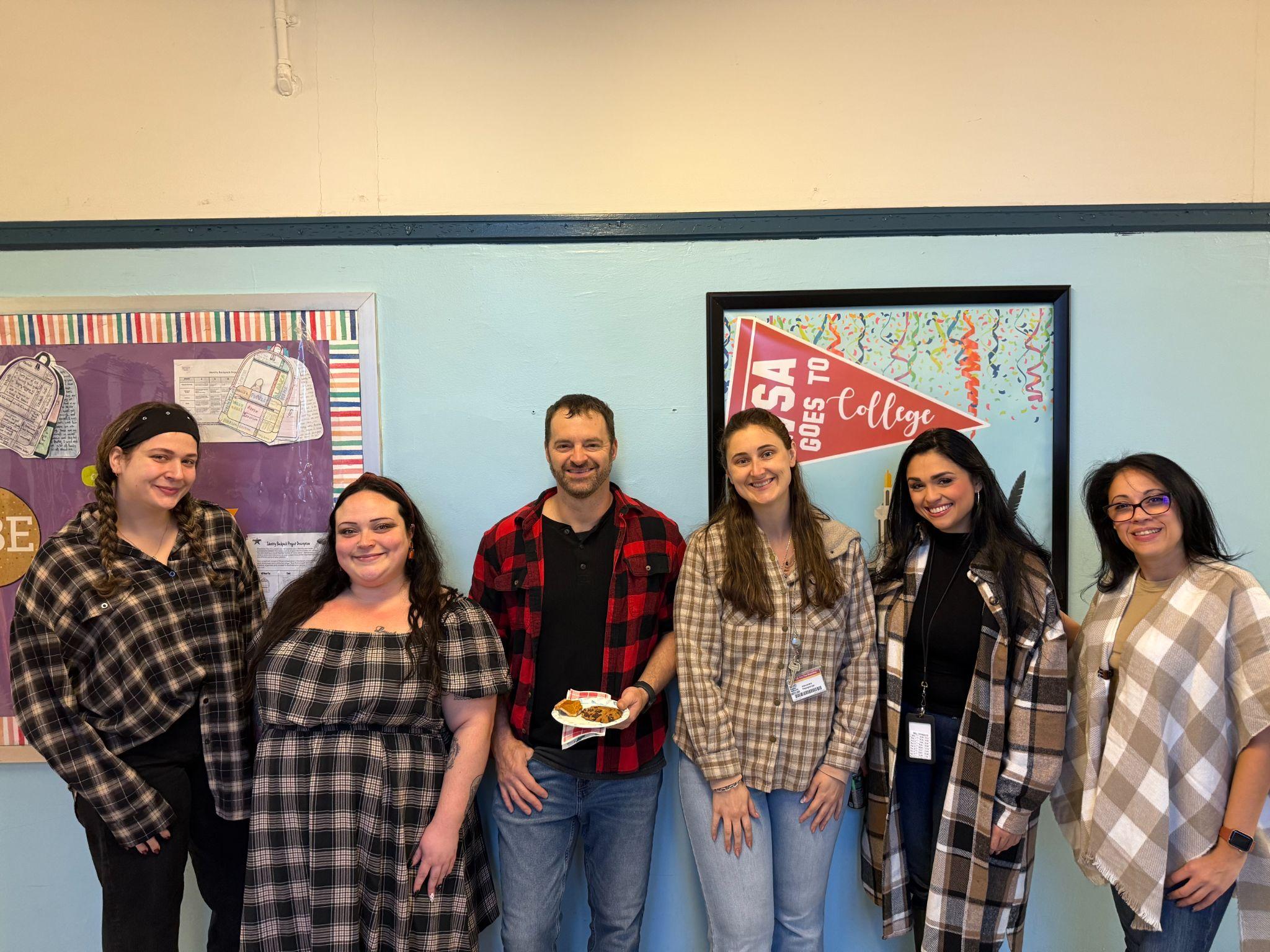 Six staff members posing together near a college bulletin board