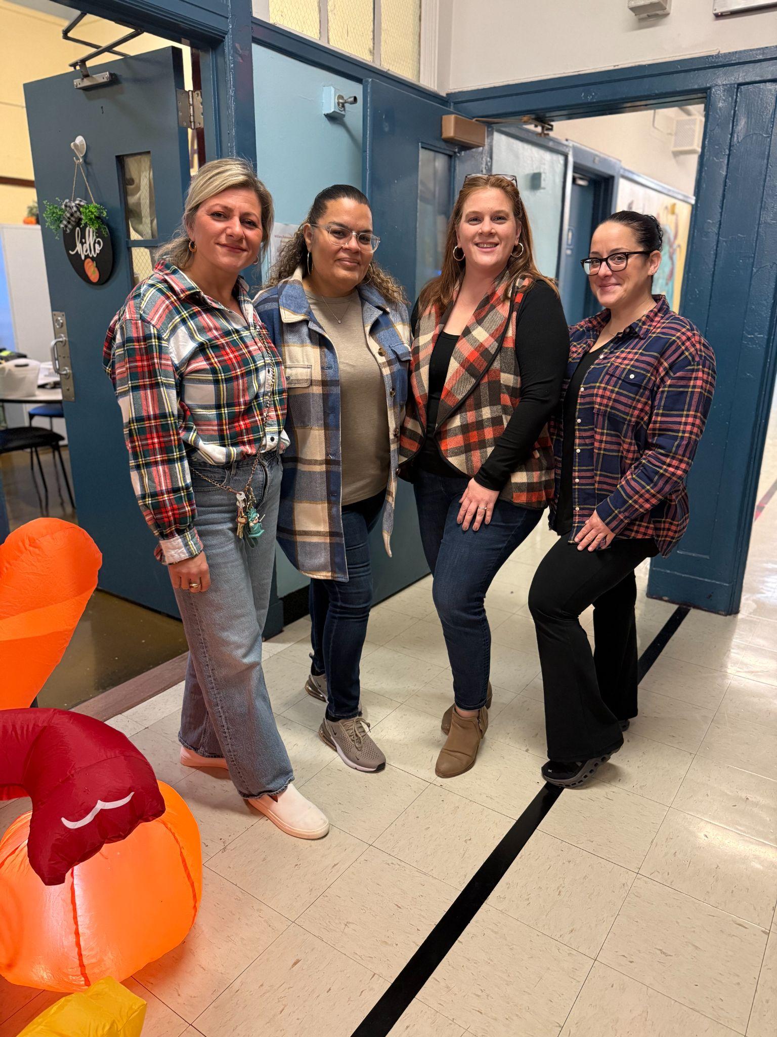 Four staff members posing together in school hallway wearing flannel
