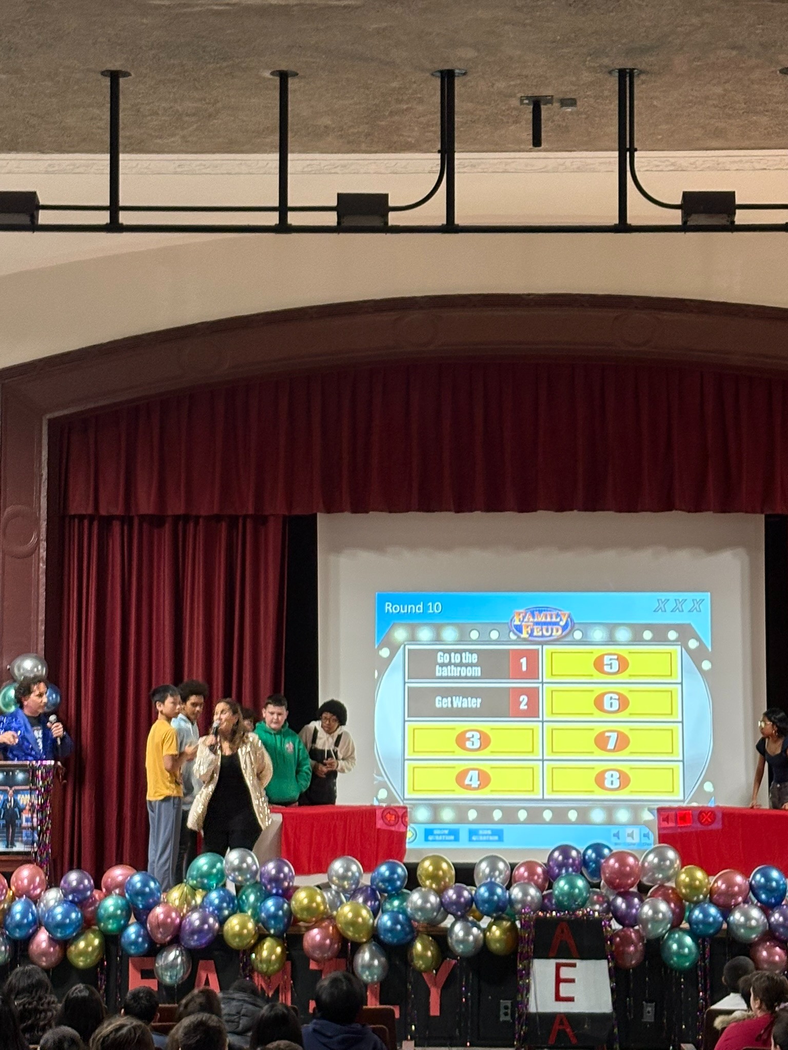 Students competing in a Family Feud game show on school stage
