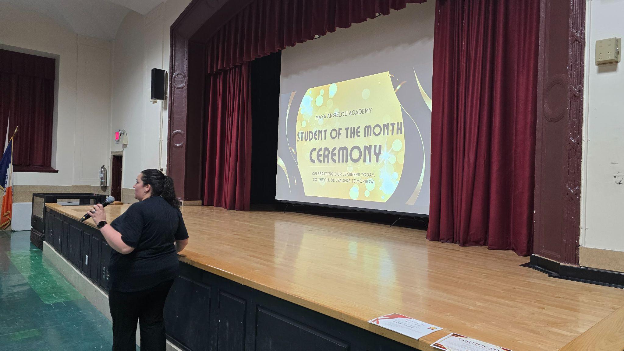 Staff member presenting at Maya Angelou Academy Student of the Month Ceremony