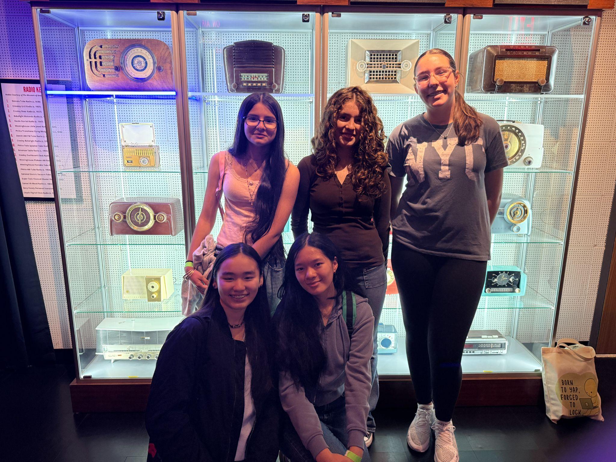 Five students posing in front of vintage radio museum display case