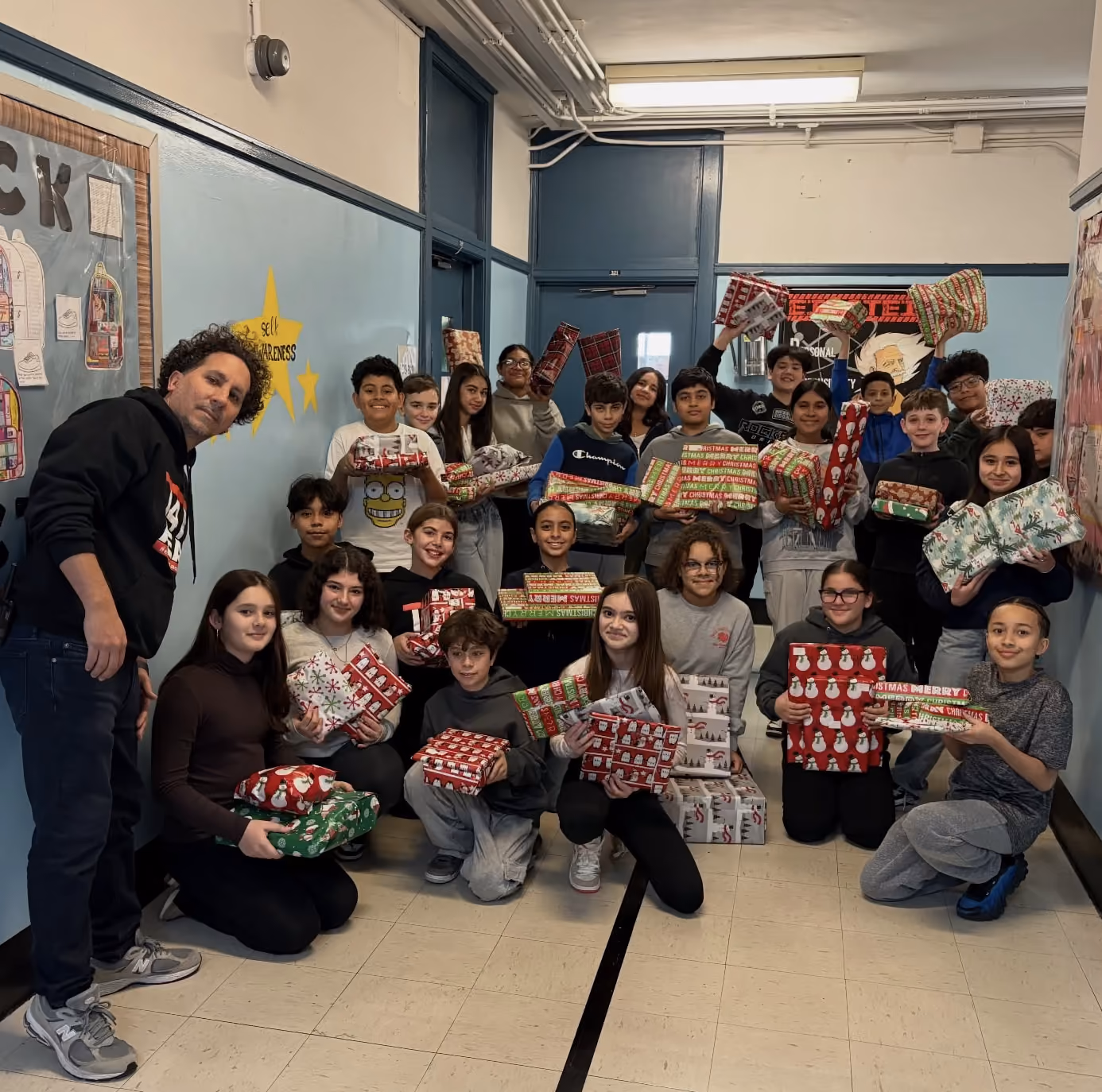 Students and teacher holding wrapped holiday gift donations in school hallway