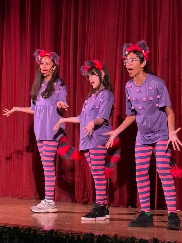 Three students in Cheshire Cat costumes performing on stage