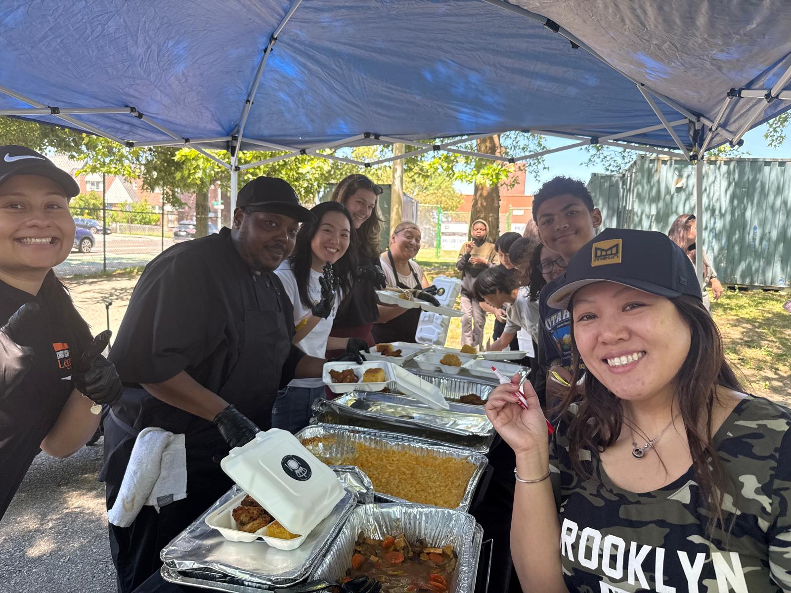Volunteers serving food at an outdoor community event under a tent