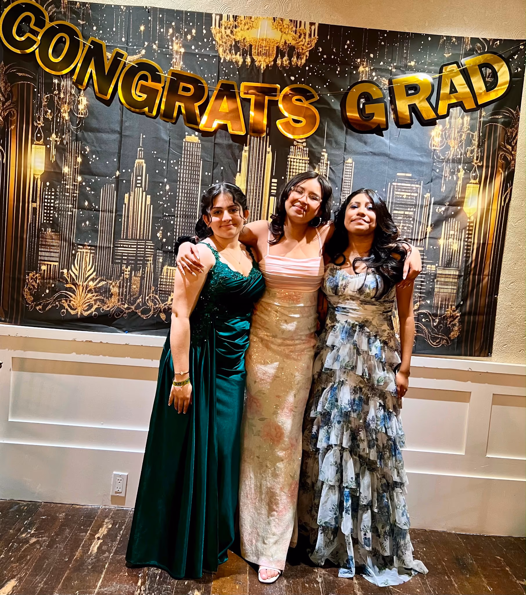 Three students in formal gowns posing at graduation celebration