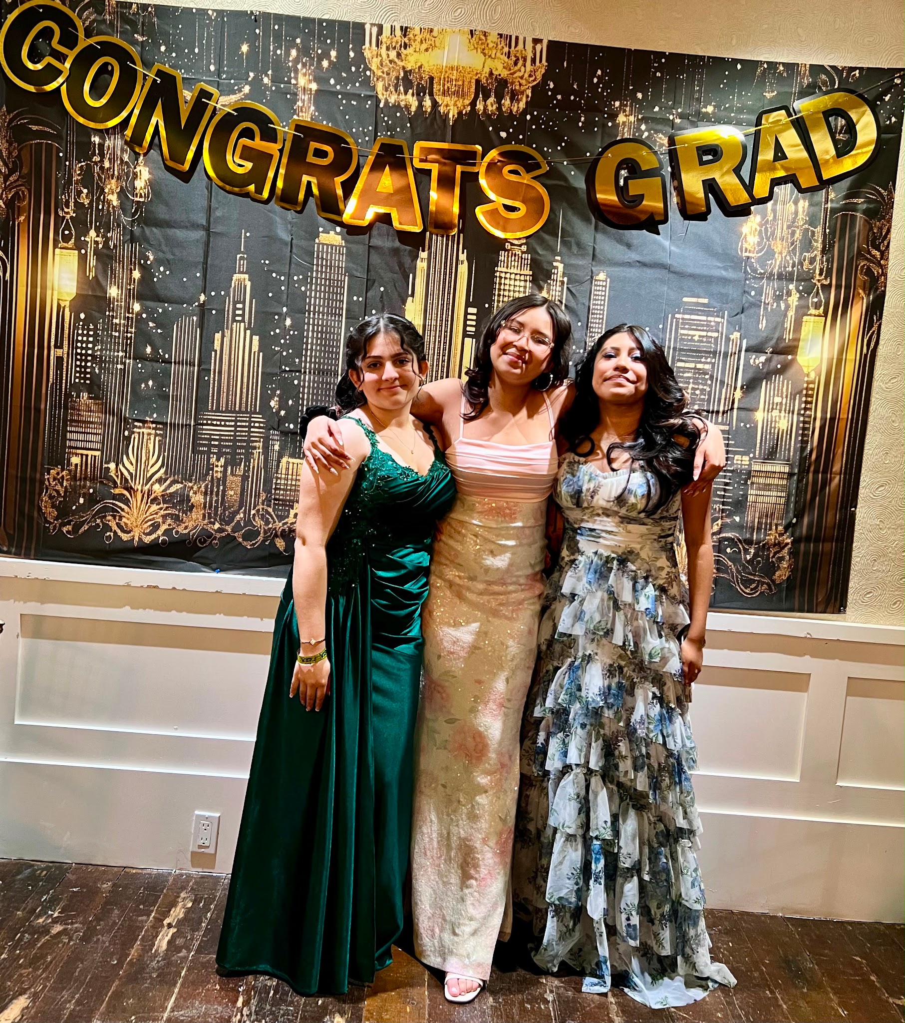 Three students in formal gowns posing at graduation celebration