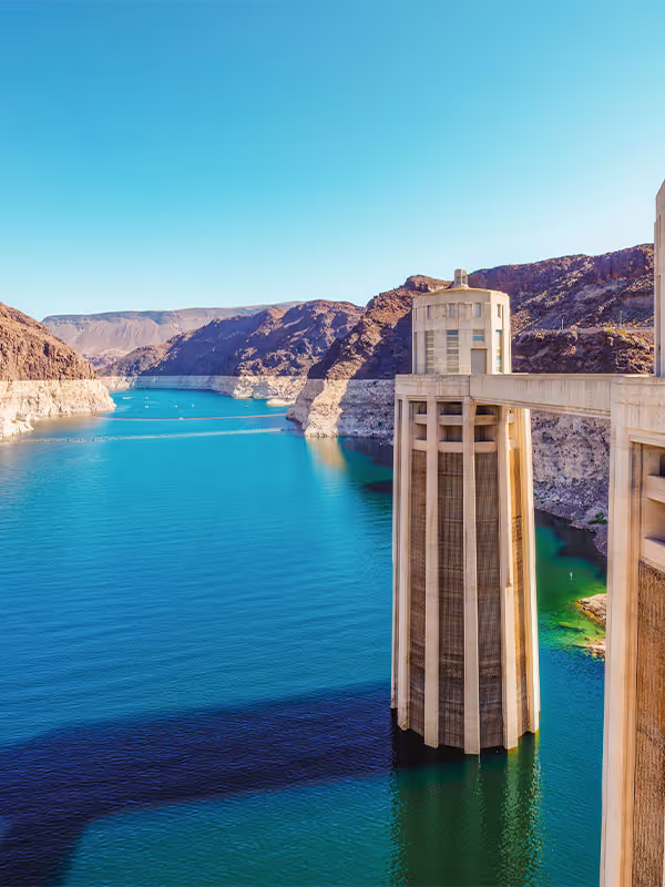 Hoover Dam intake tower above blue water with rocky desert mountains in the background under clear sky.