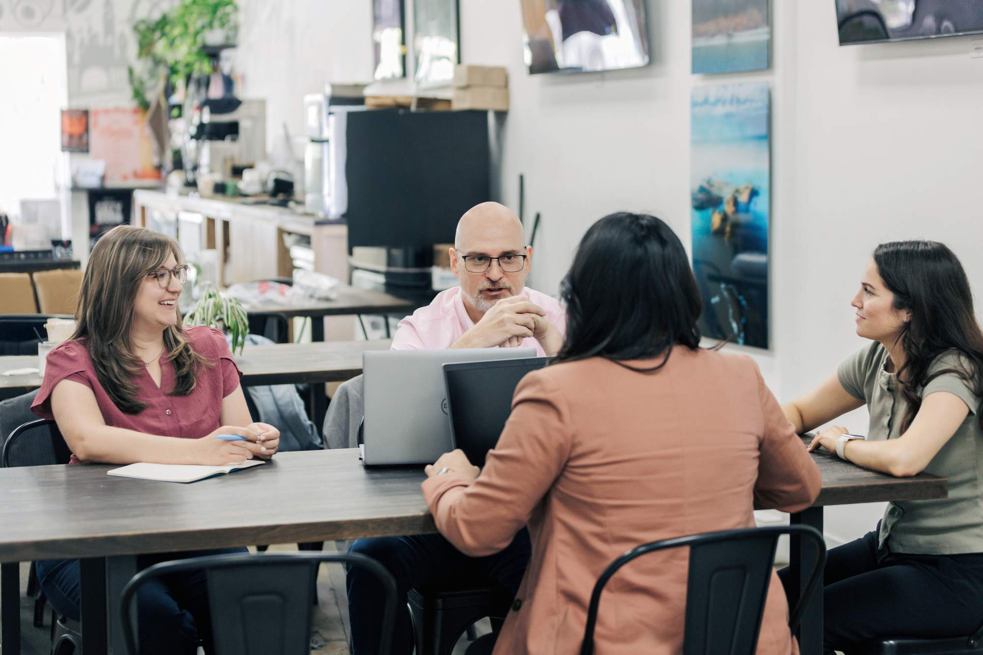 Four Biplane team members having a discussion around a wooden table in a modern office setting, with two laptops open and notebooks on the table.