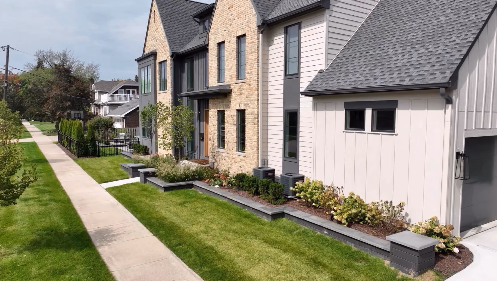 Modern house front yard with green lawn, sidewalk, garden beds, and brick with siding exterior.