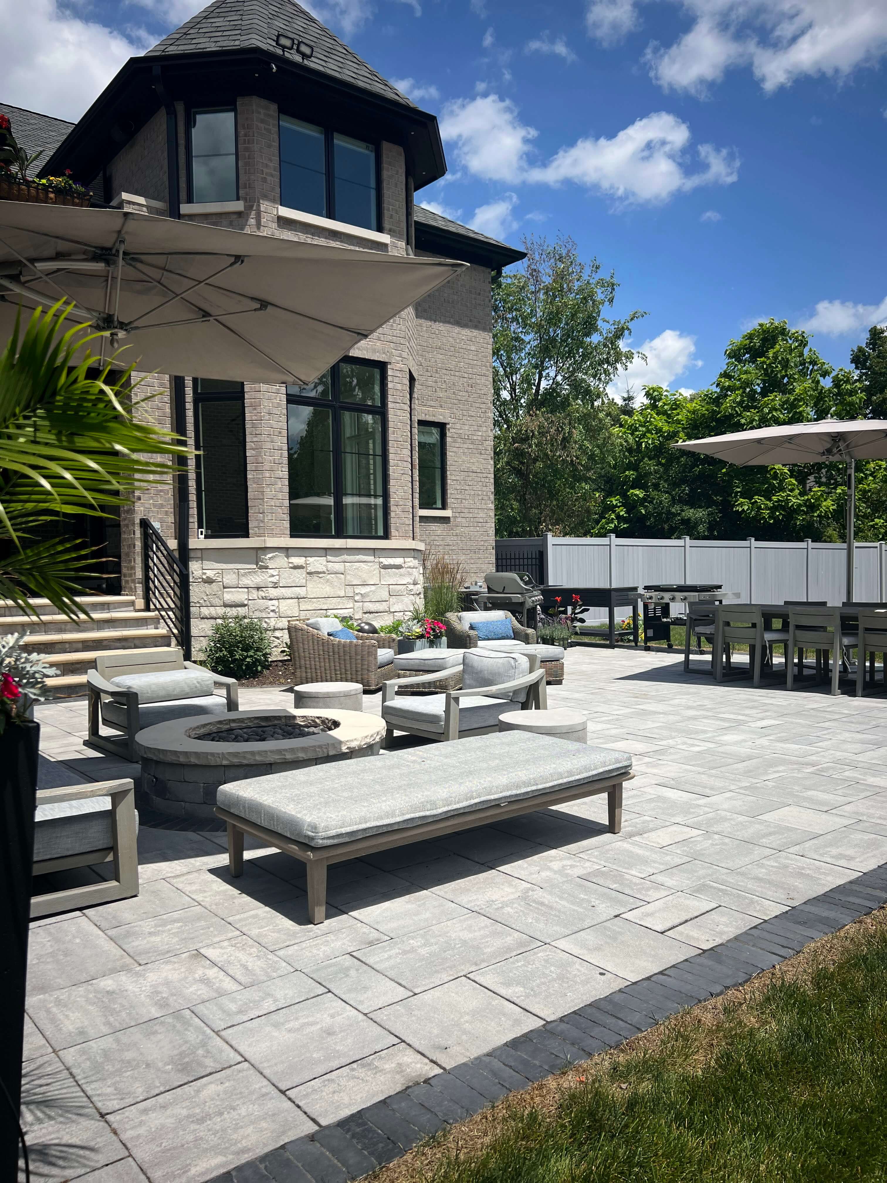 Spacious backyard patio with gray stone flooring, cushioned seating, umbrellas, and a fire pit.