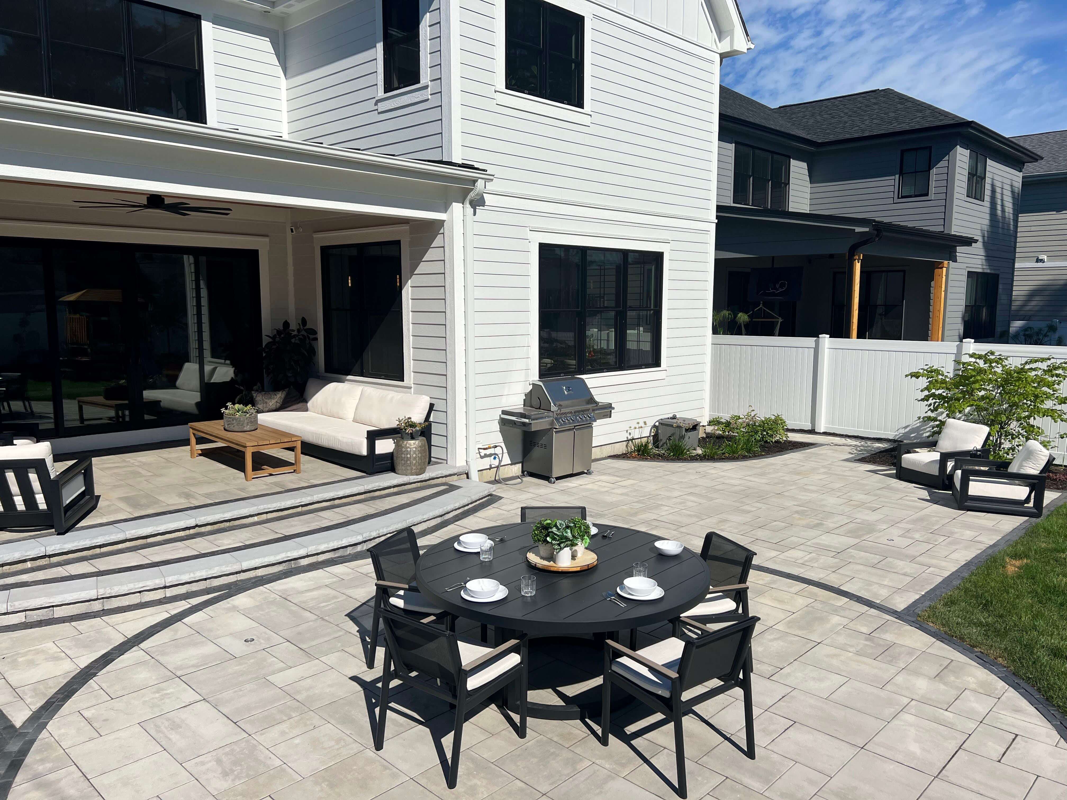 Modern white house backyard patio with black dining table, chairs, lounge seating, and gas grill.