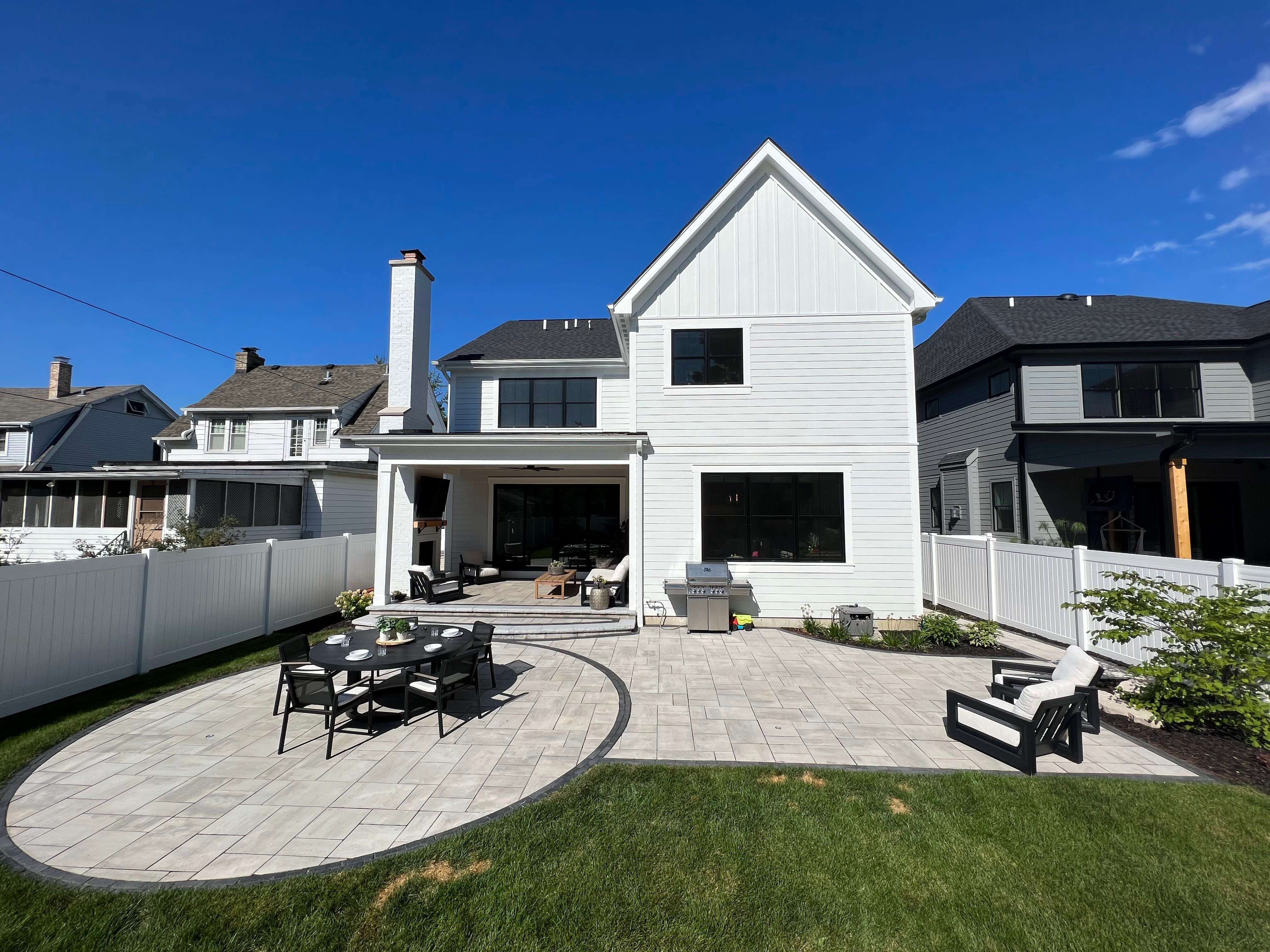 White two-story house with a backyard patio featuring a dining set and outdoor chairs on stone flooring.