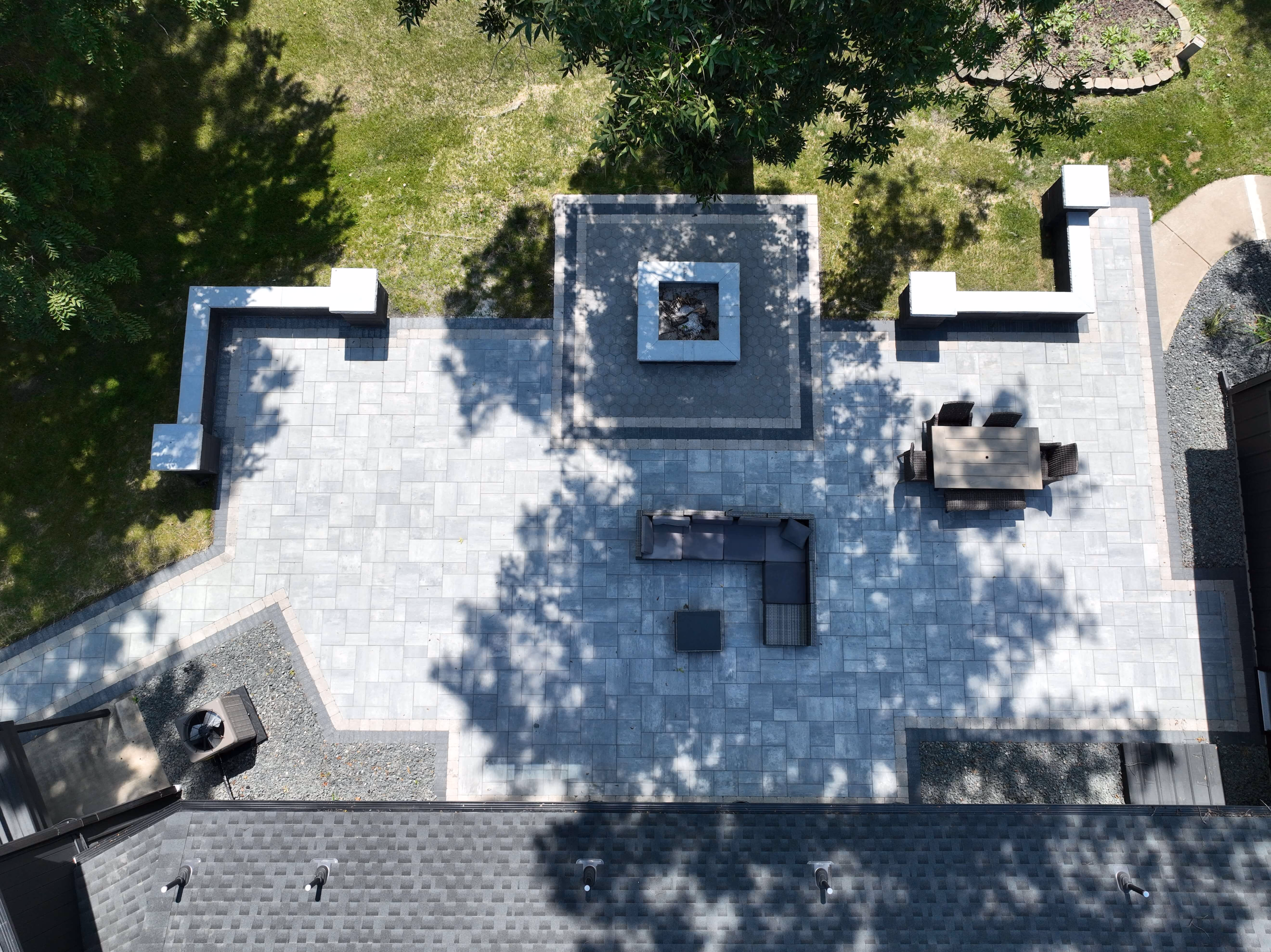 Aerial view of backyard patio with stone tiles, fire pit, outdoor sofa, and dining table with chairs.