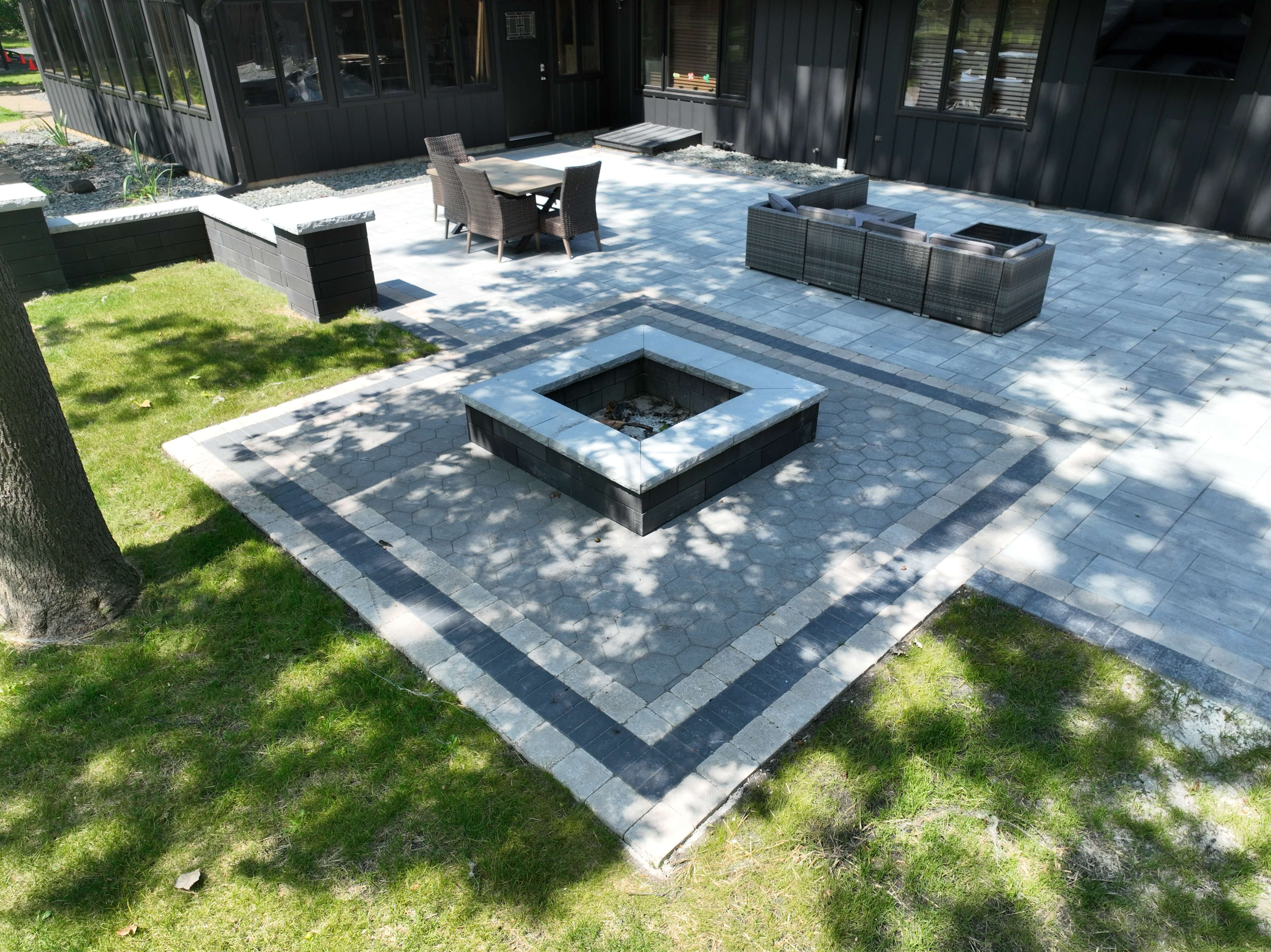 Modern backyard patio with stone fire pit, seating area, dining table, and black house exterior.