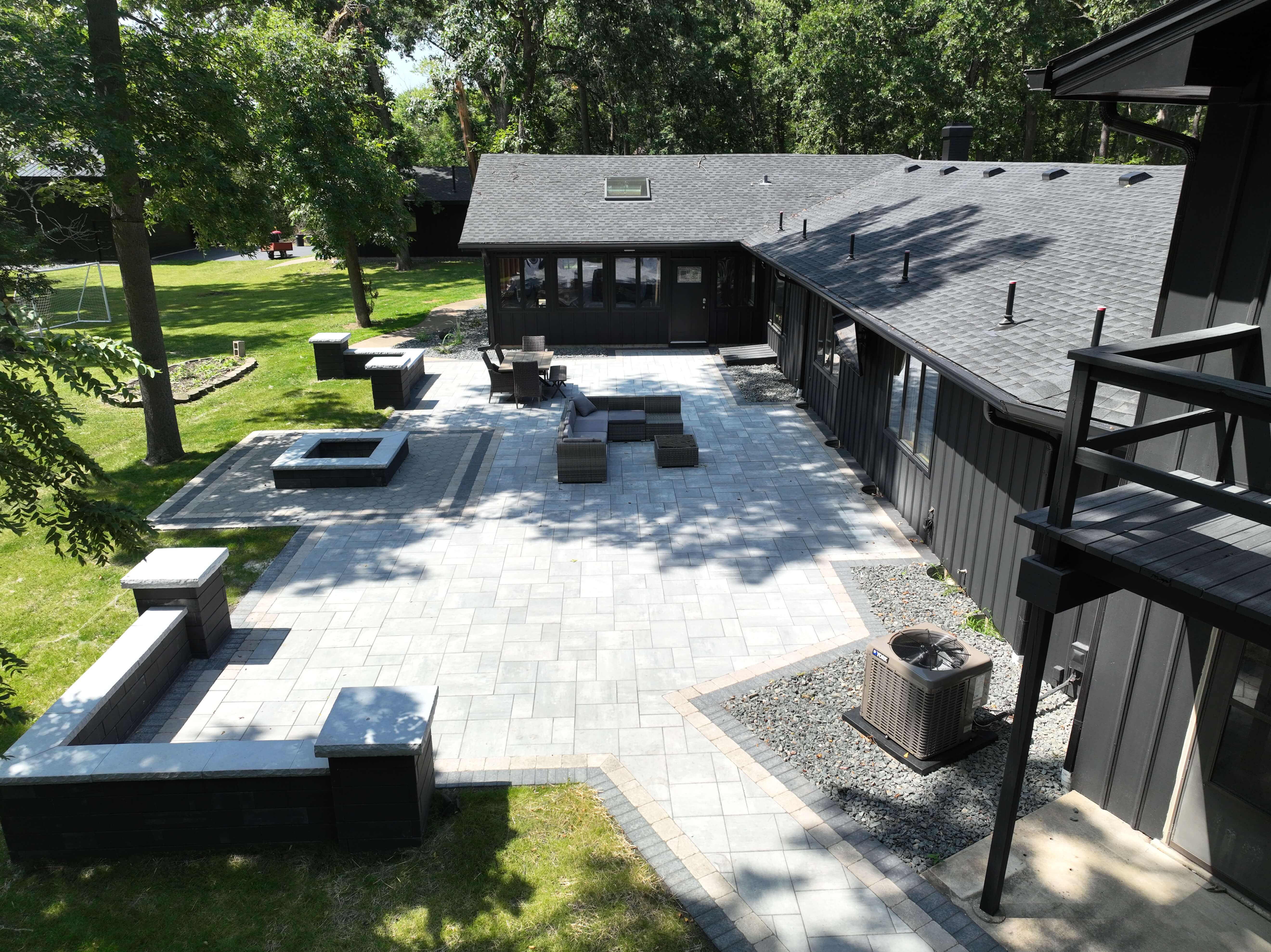 Backyard patio with light stone pavers, seating area, fire pit, and dark wood house exterior.