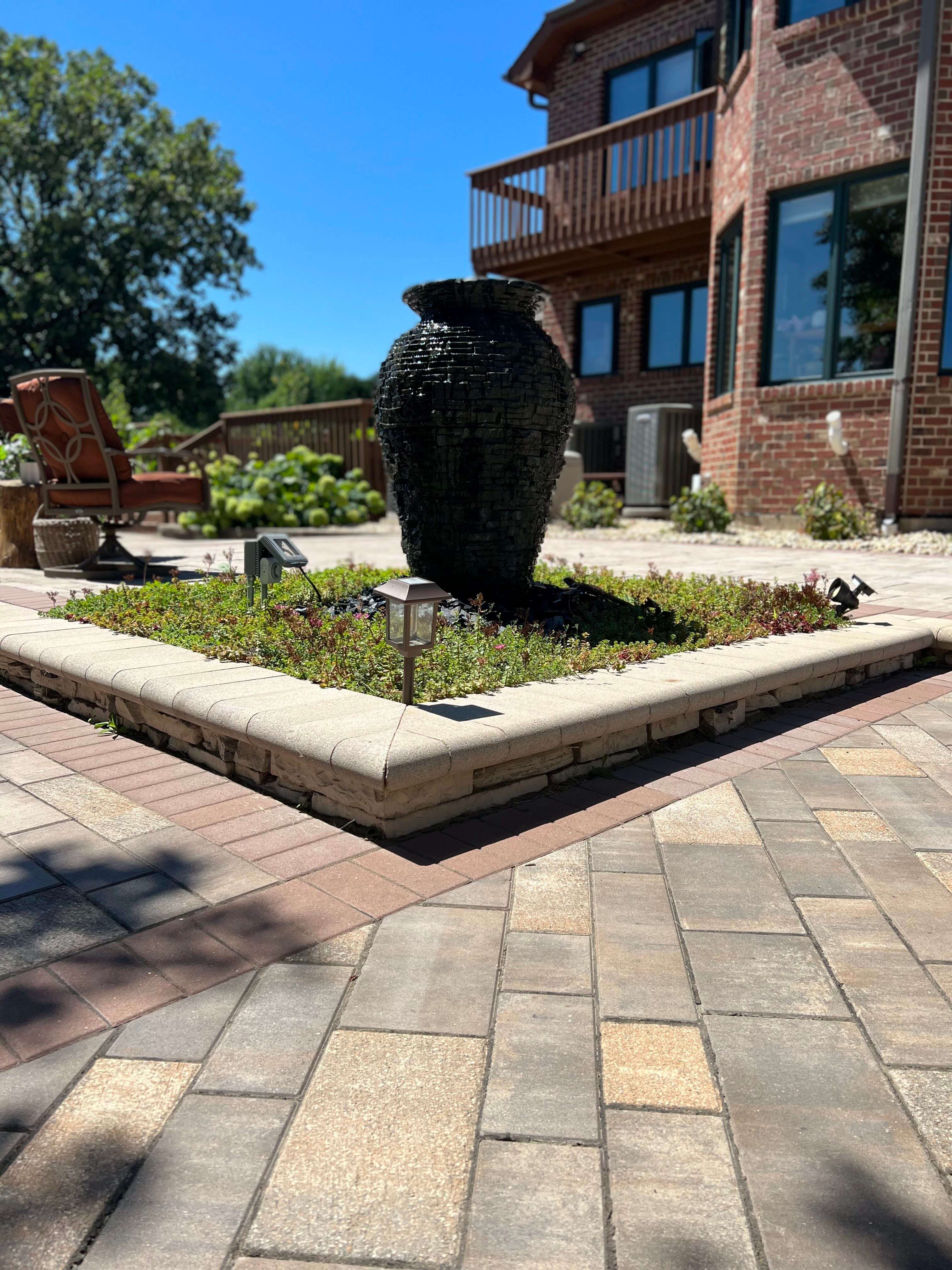 Patio with brick pavers, a raised planter with greenery, and a large black urn water feature.
