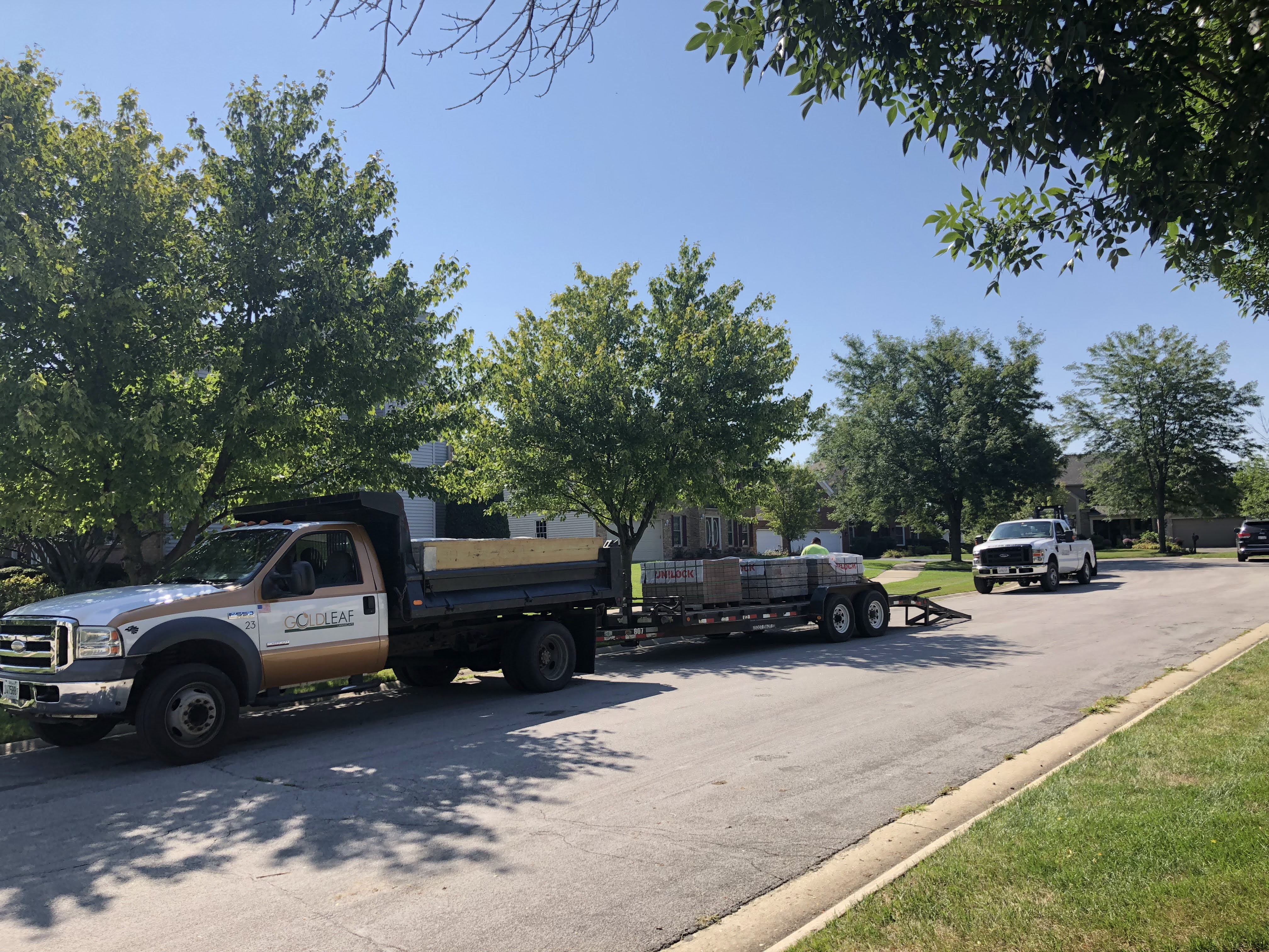 Goldleaf truck with trailer loaded with bricks parked on a suburban street on a sunny day.