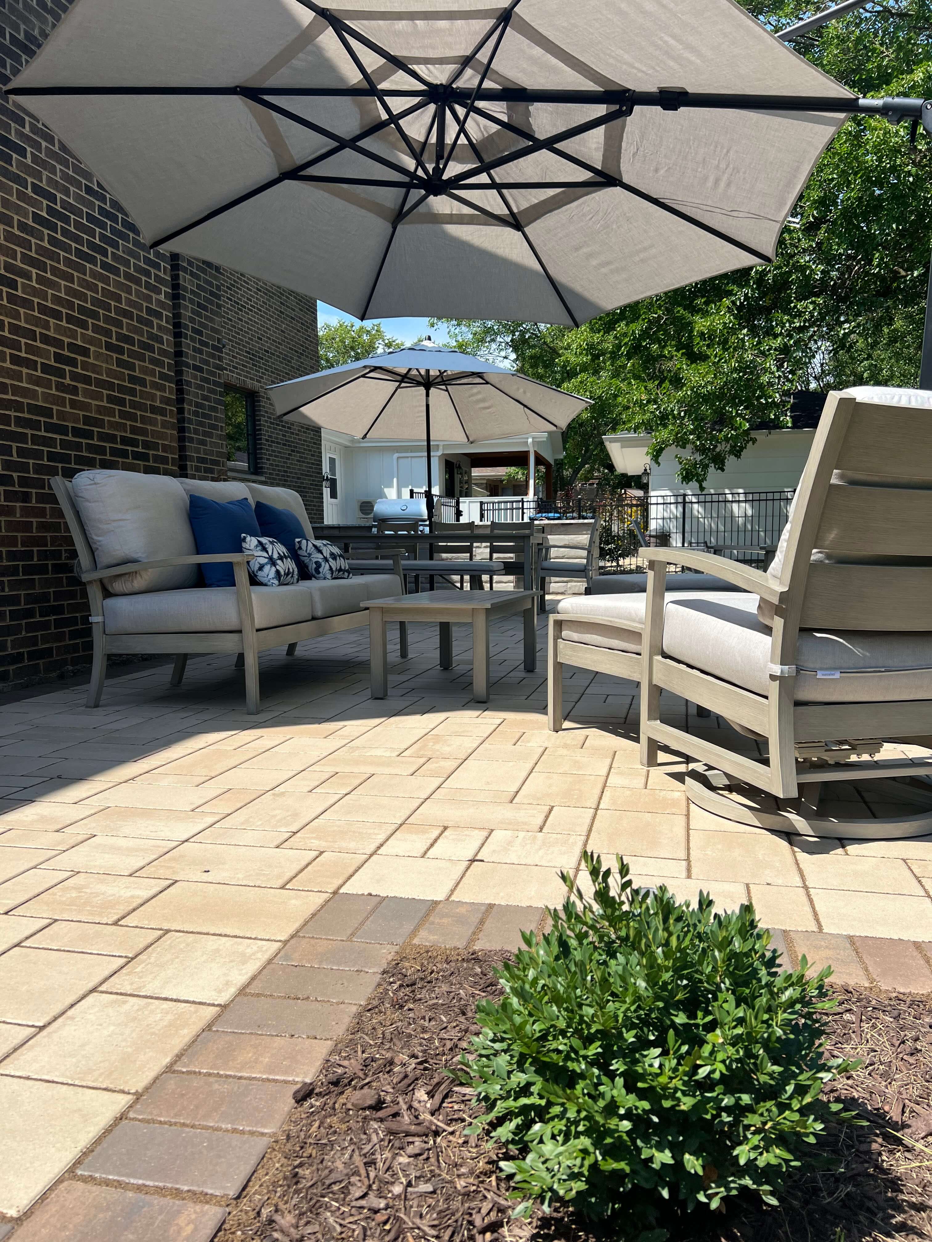Aerial view of a brick backyard patio with two umbrellas, outdoor seating, firepit, and grill area.