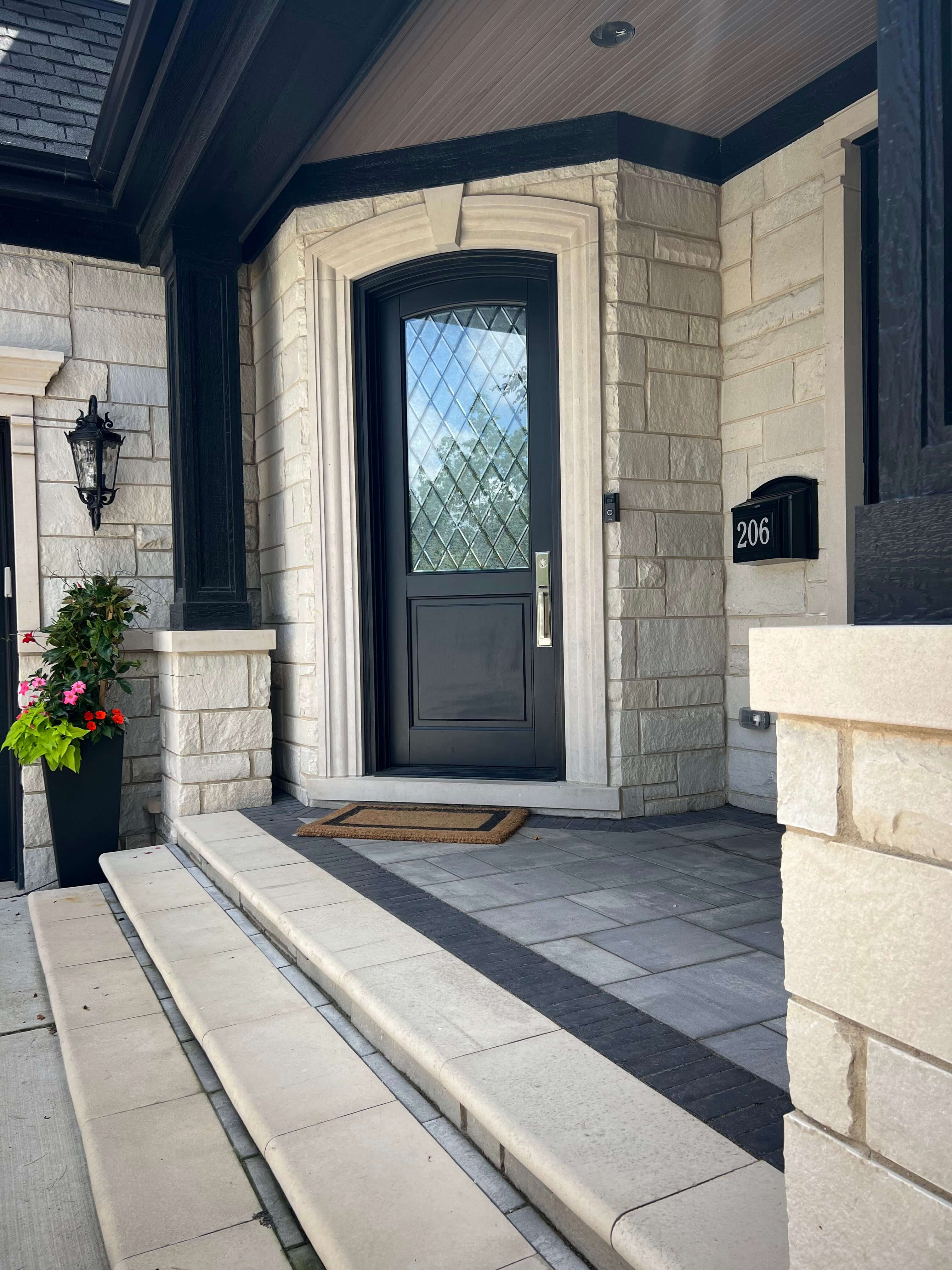 Front steps leading to a black front door with diamond-patterned glass and stone exterior walls.