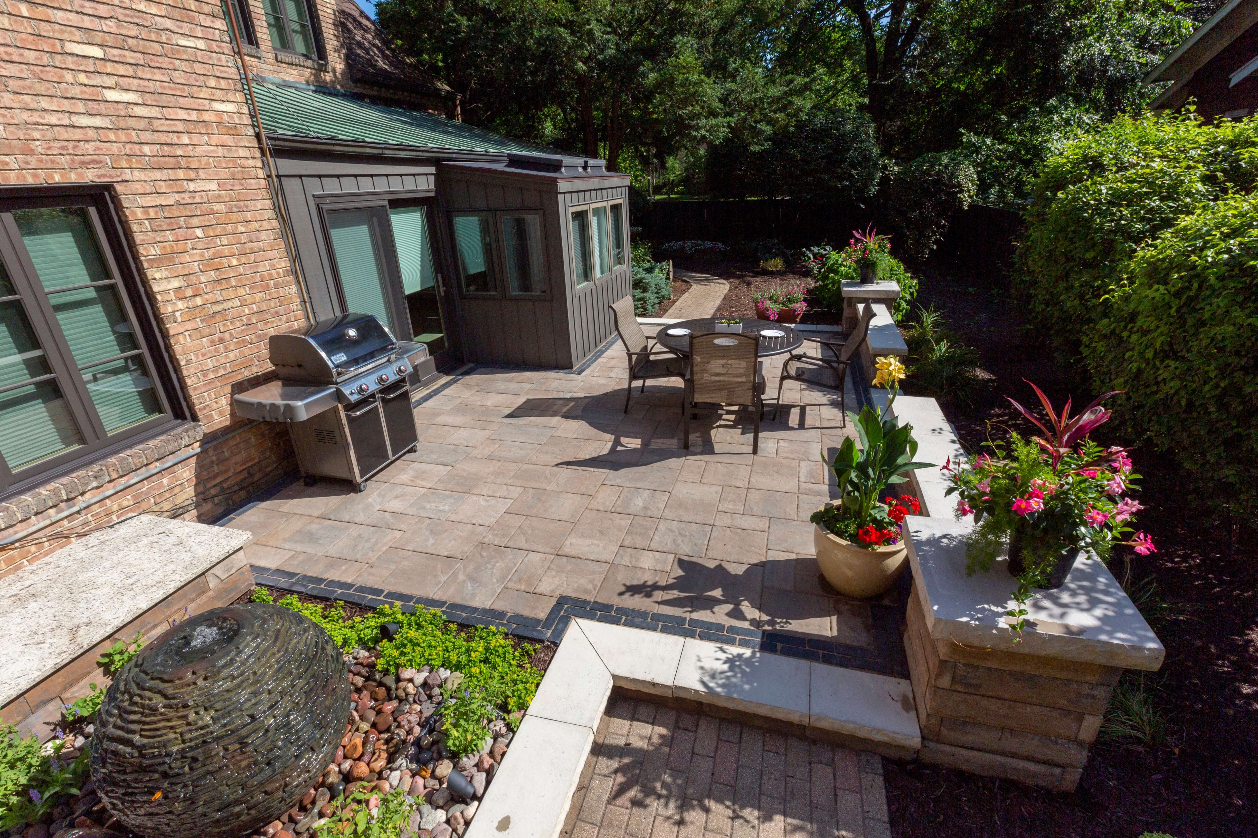 Aerial view of a backyard patio with stone tiles, fire pit, outdoor sofa, and dining table with chairs.