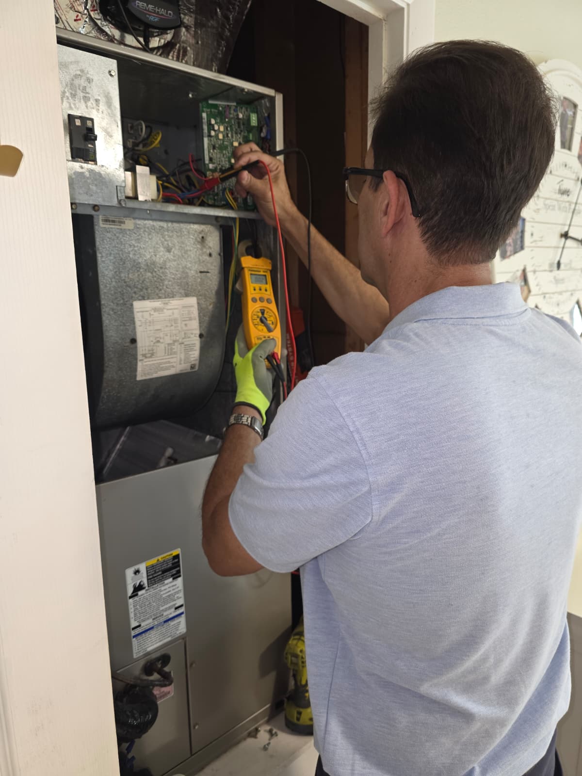 Technician in light blue shirt uses a multimeter to test wiring inside an HVAC unit.