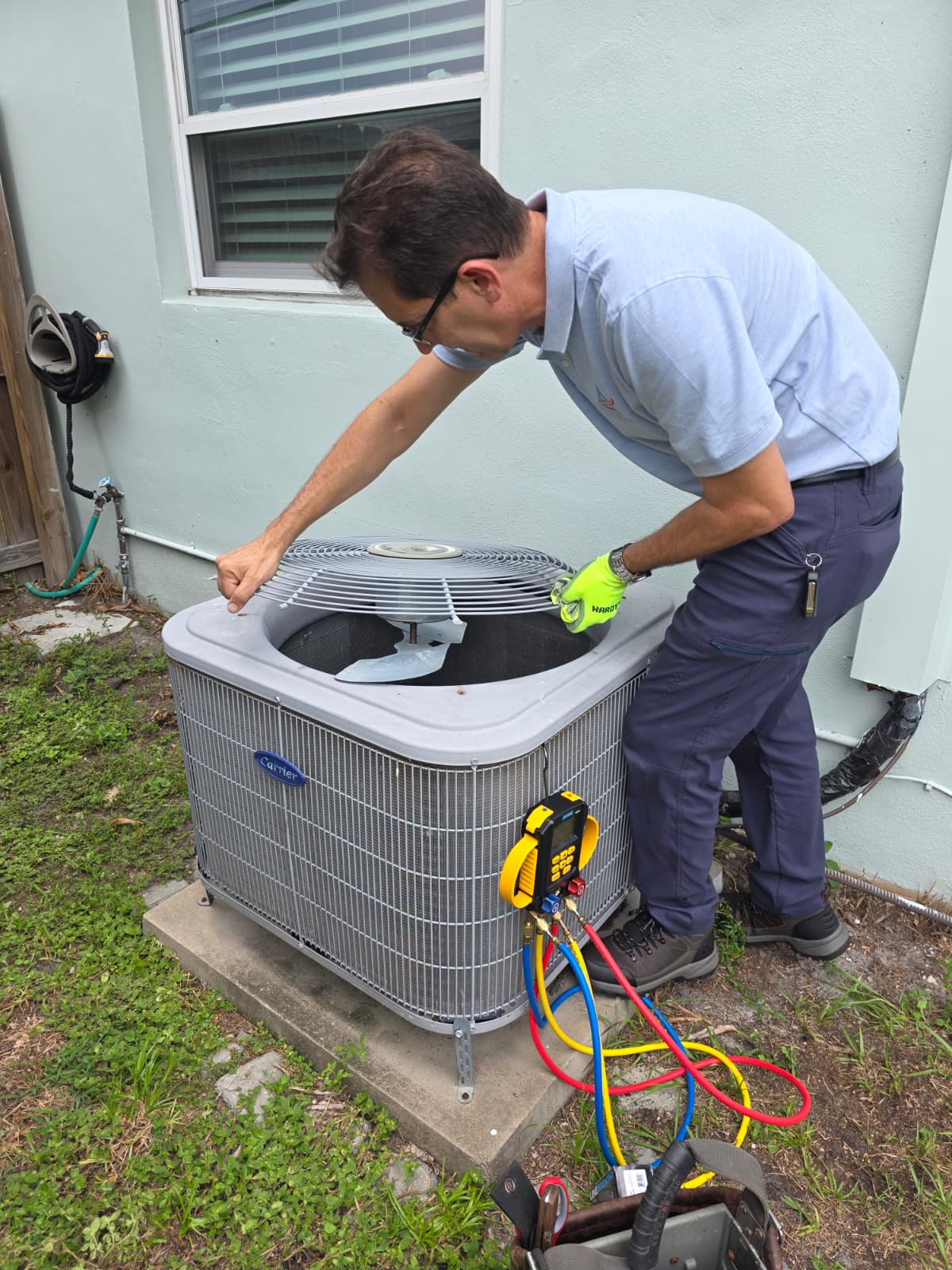 Technician in gloves inspecting an outdoor Carrier air conditioning unit with gauges attached.