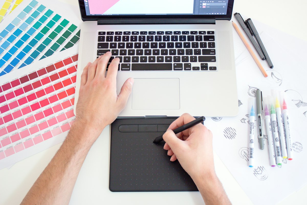 Graphic designer working on a laptop with color swatches and a digital tablet