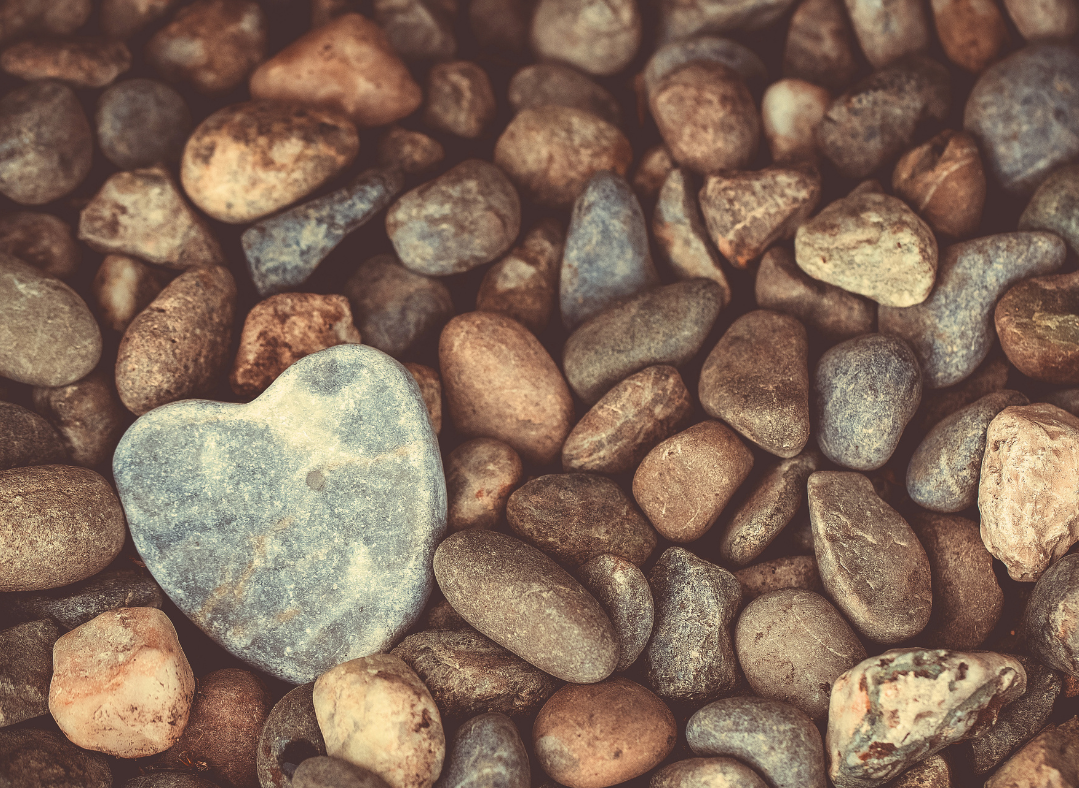 A group of natural stones in shades of red, brown, and gray with one larger stone with a shape resembling a heart.
