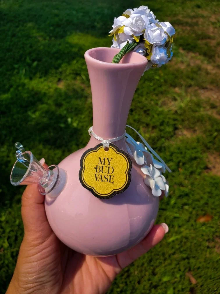 Hand holding a pink ceramic bud vase with white flowers and a yellow tag reading My Bud Vase.