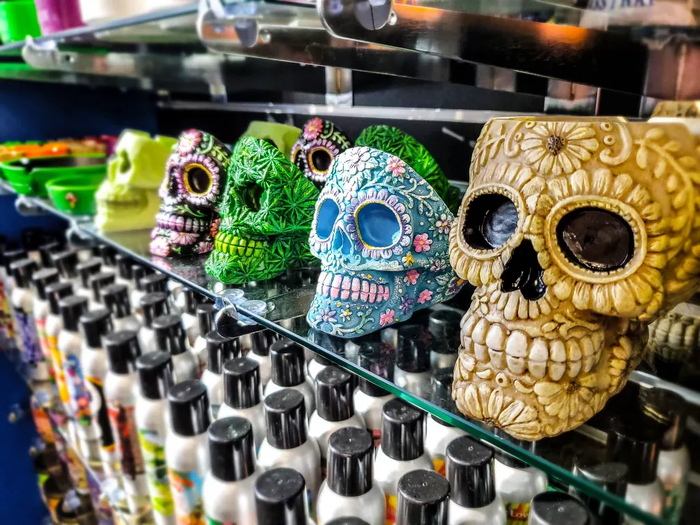 Colorful decorative skulls with intricate floral patterns on a glass shelf above bottles.