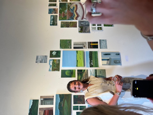 Lara standing beside a wall of her framed paintings