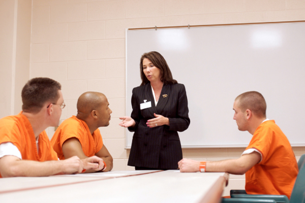 A pharmaceutical representative speaking in a classroom setting to individuals wearing orange correctional uniforms.