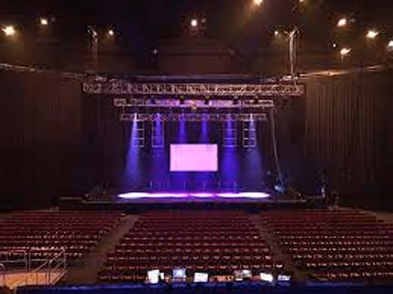 Empty auditorium with rows of seats facing a stage lit in purple with a large blank screen.