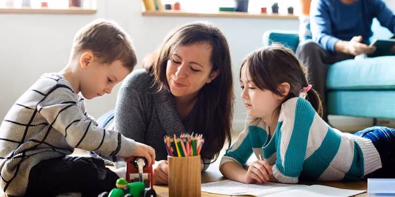 Woman lying on the floor with two children, one playing with a toy car and the other drawing with colored pencils.